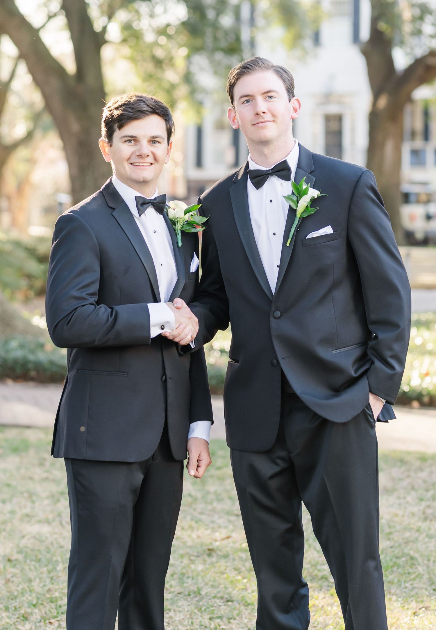 Groomsmen in black tuxedos share candid moments during outdoor wedding photos.
