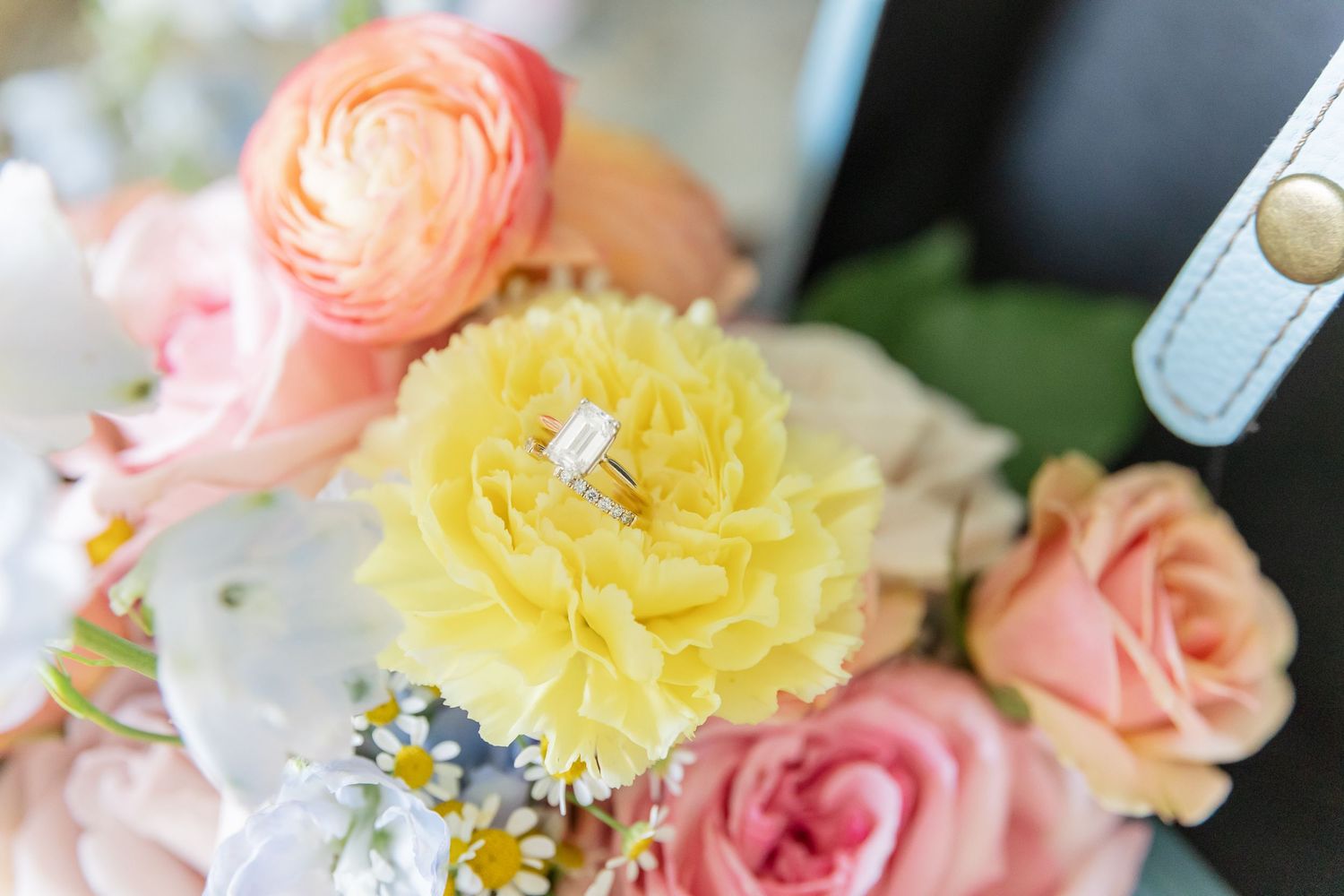 Close-up of a pastel wedding bouquet featuring pink ranunculus, yellow flowers, and delicate white blooms.