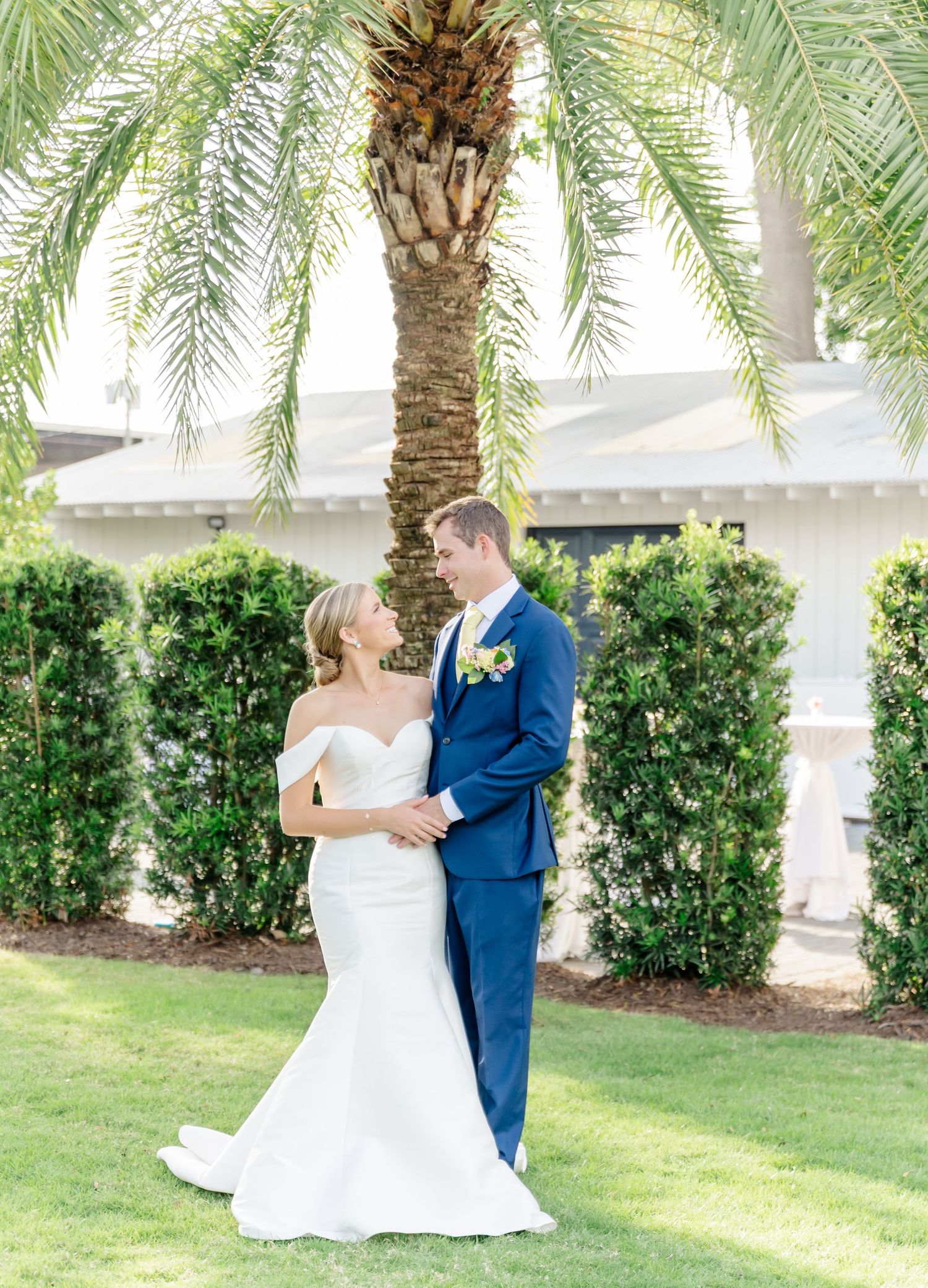 A couple in wedding attire embraces under palm trees in a tropical garden setting.