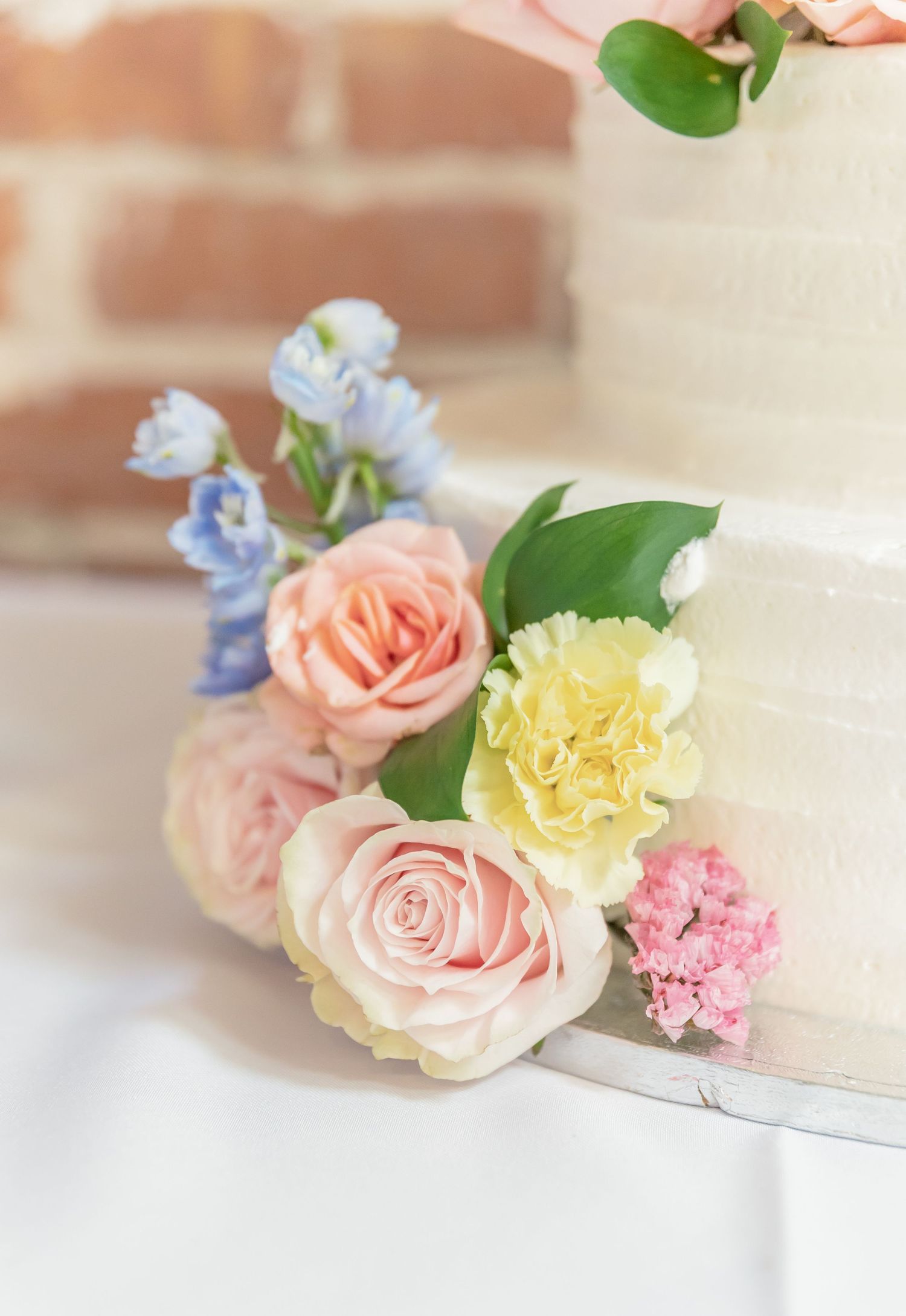 Delicate pastel roses and carnations arranged in a soft gradient from pink to yellow against a light background.