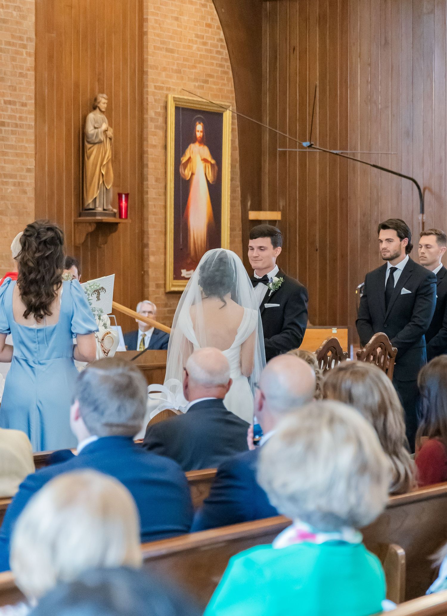 Wedding ceremony in progress inside a church with wooden panels and religious artwork on display.