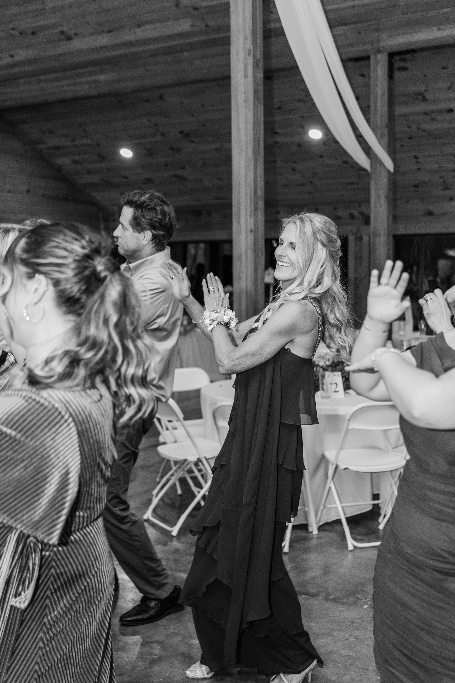 Wedding guests dance and celebrate in black and white at a rustic reception venue.