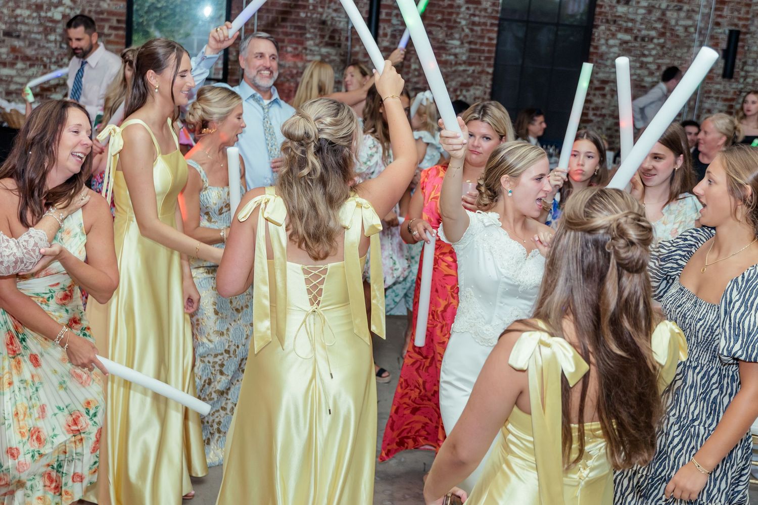 A group of people in yellow and floral dresses dancing and celebrating at a festive gathering.