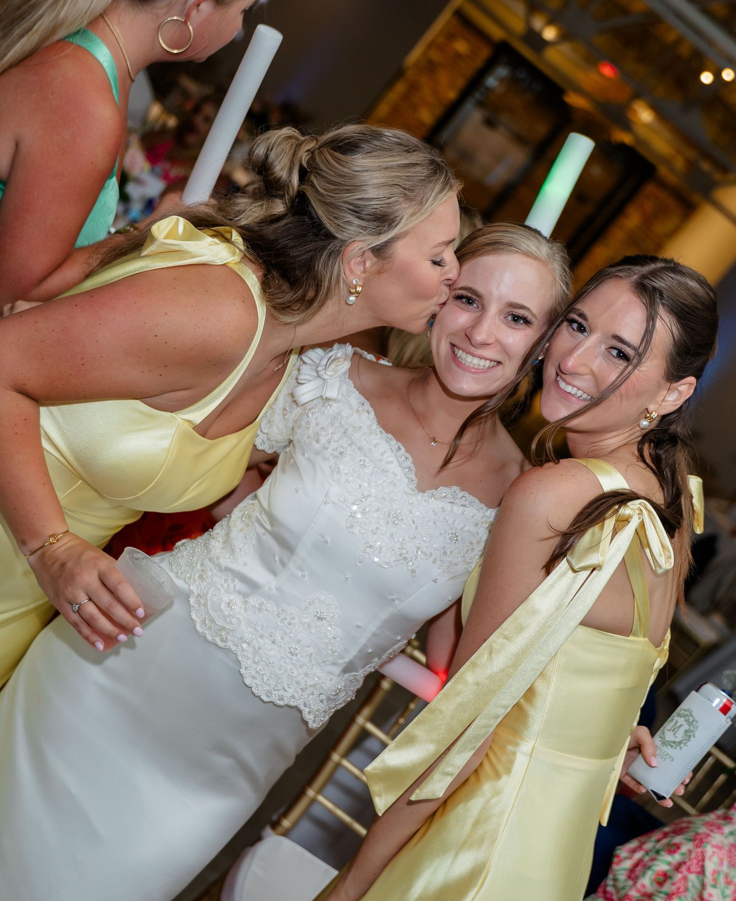 Bridesmaids in pale yellow dresses share joyful moments with the bride in a white lace gown at the reception.