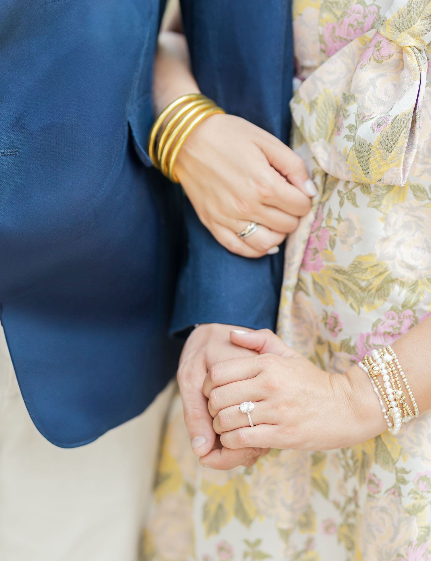 Close-up of hands wearing gold bangles and diamond rings against navy blue and floral print fabrics.