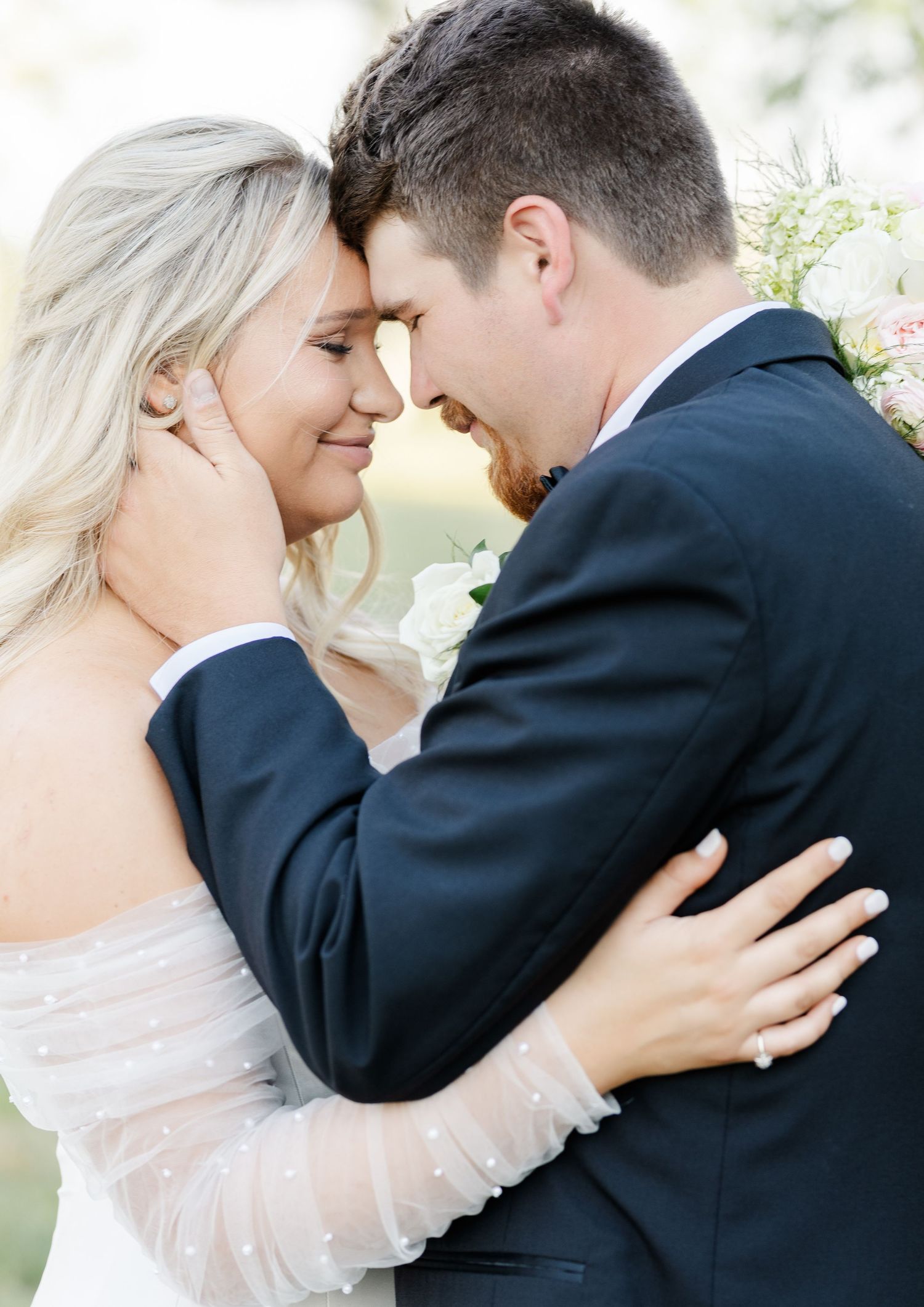 Bride and groom touching foreheads tenderly, bride wearing off-shoulder dotted tulle wedding dress.