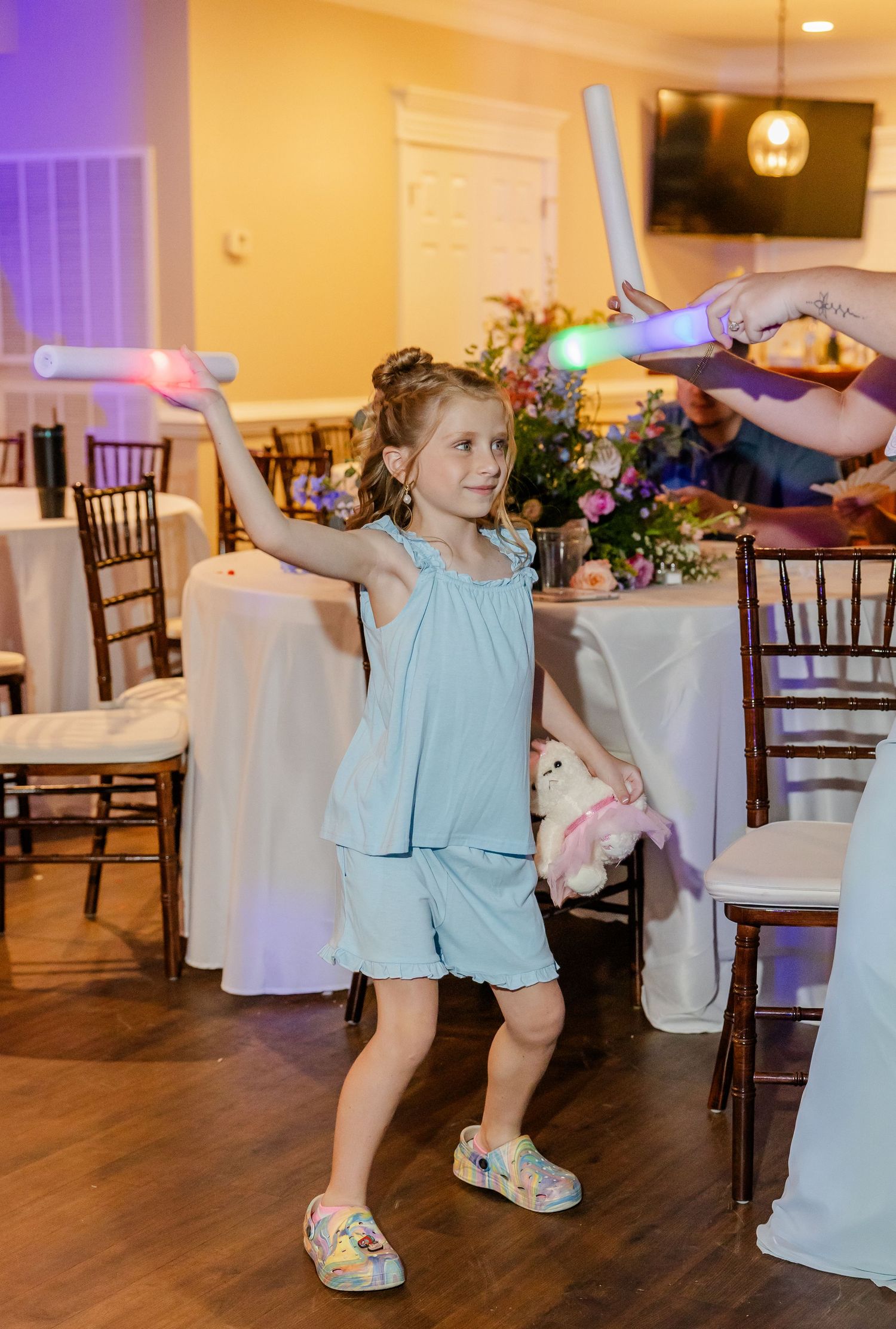 Young flower girl dances with a glow stick at the wedding reception in a light blue outfit.