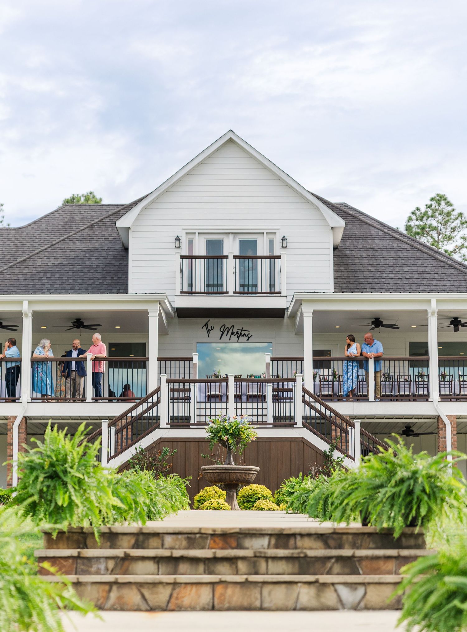 Elegant white two-story wedding venue with wrap-around porch and guests mingling on balcony.