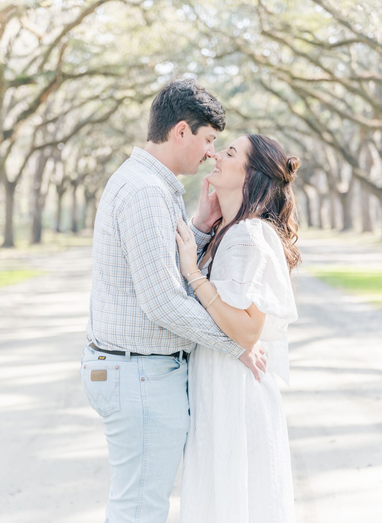 A romantic embrace shared under an enchanting canopy of oak trees on a spring day.