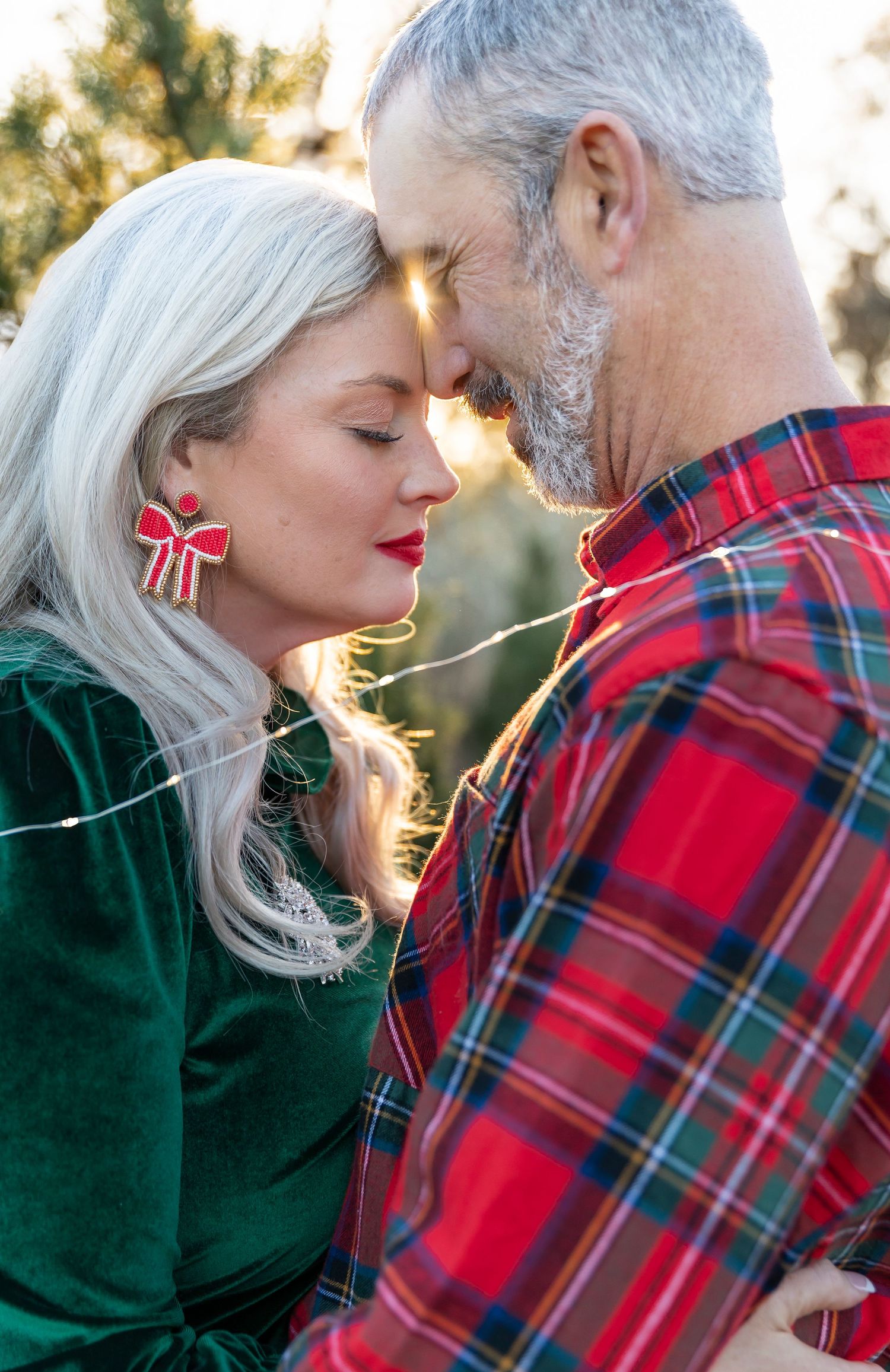 Romantic sunset portrait of couple in festive red and green holiday attire among pine trees.