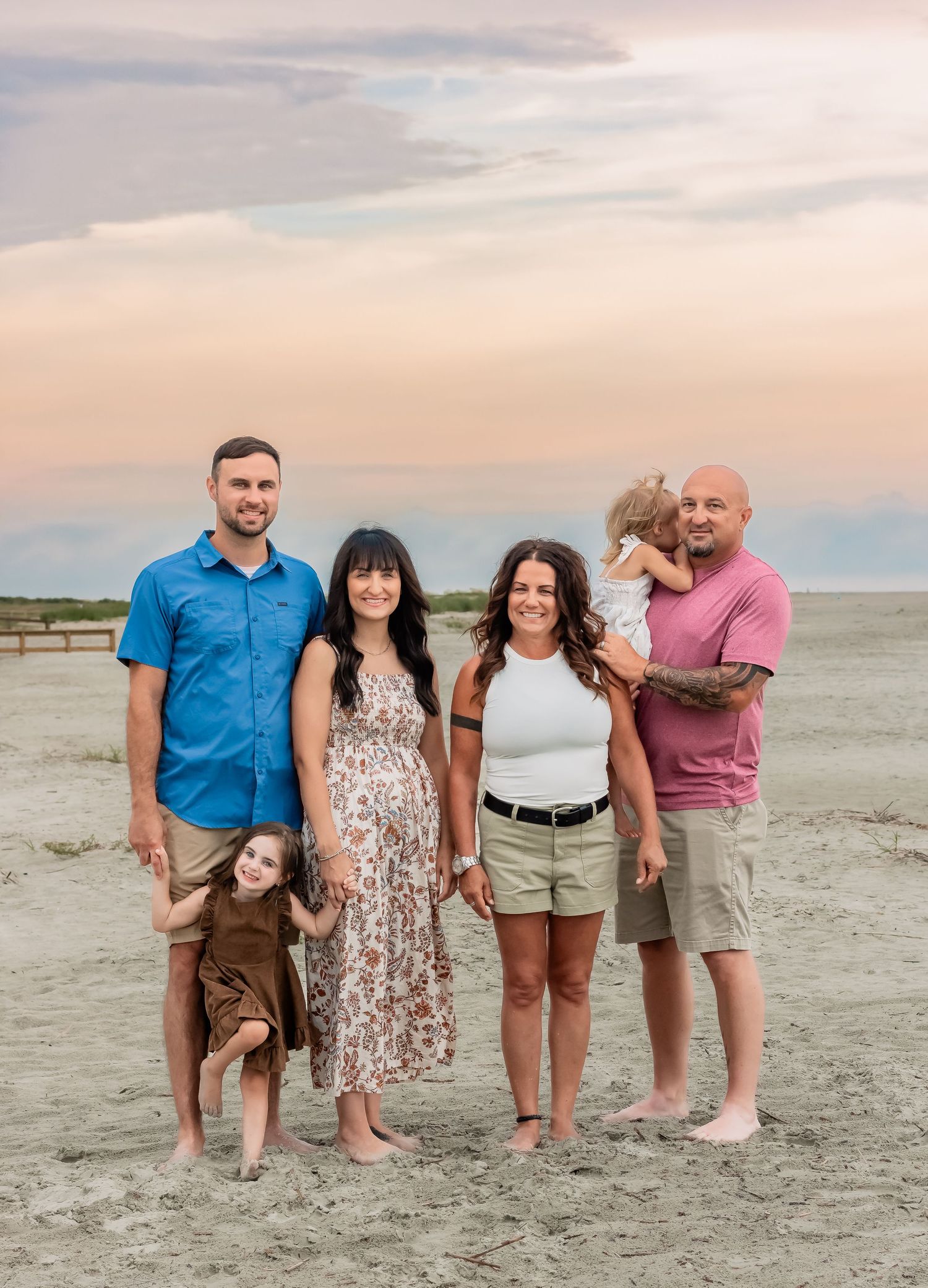 Extended family group poses together on beach at sunset in casual summer clothing.