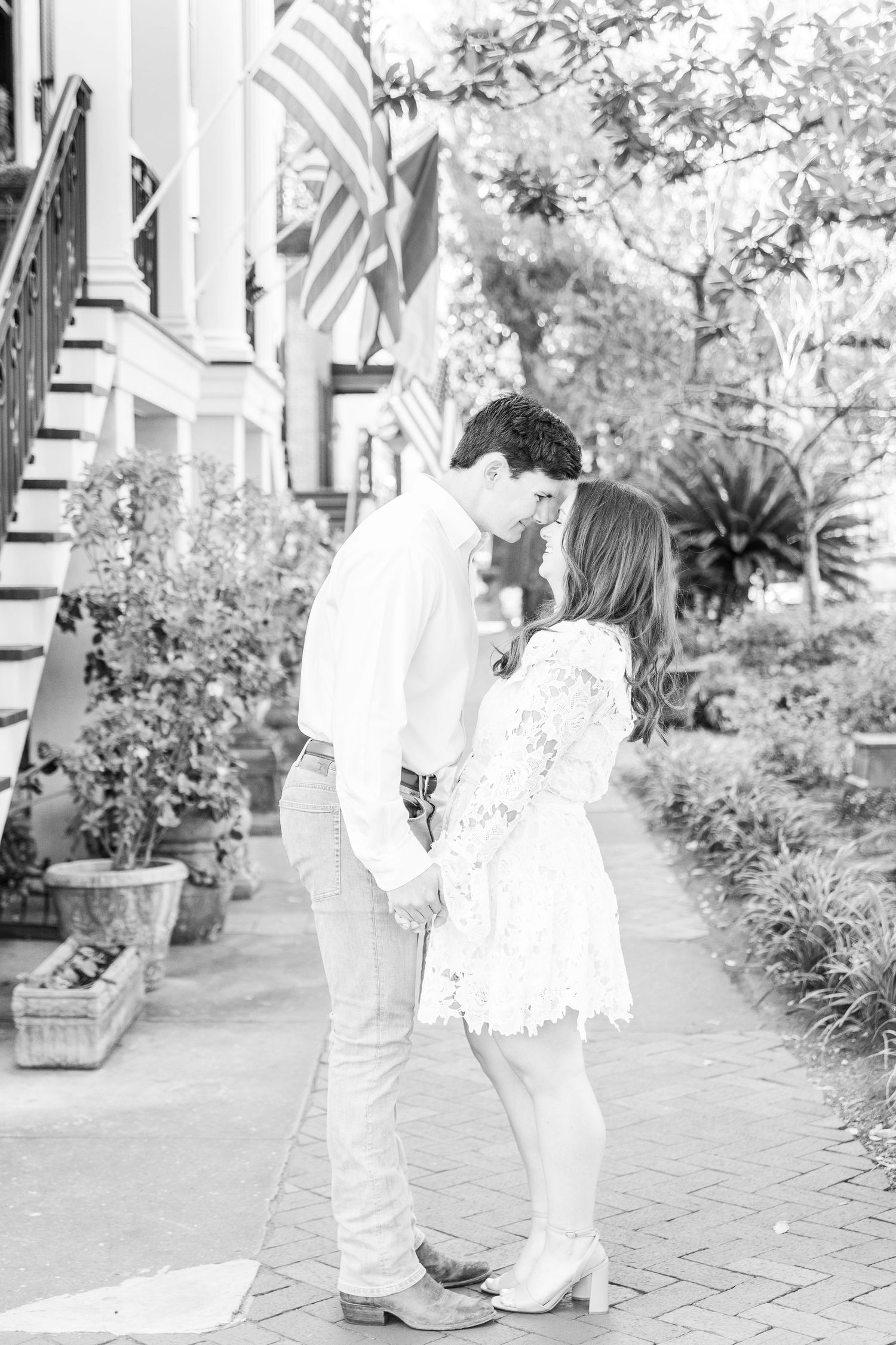 Black and white photo of couple in white outfits embracing on a brick sidewalk.
