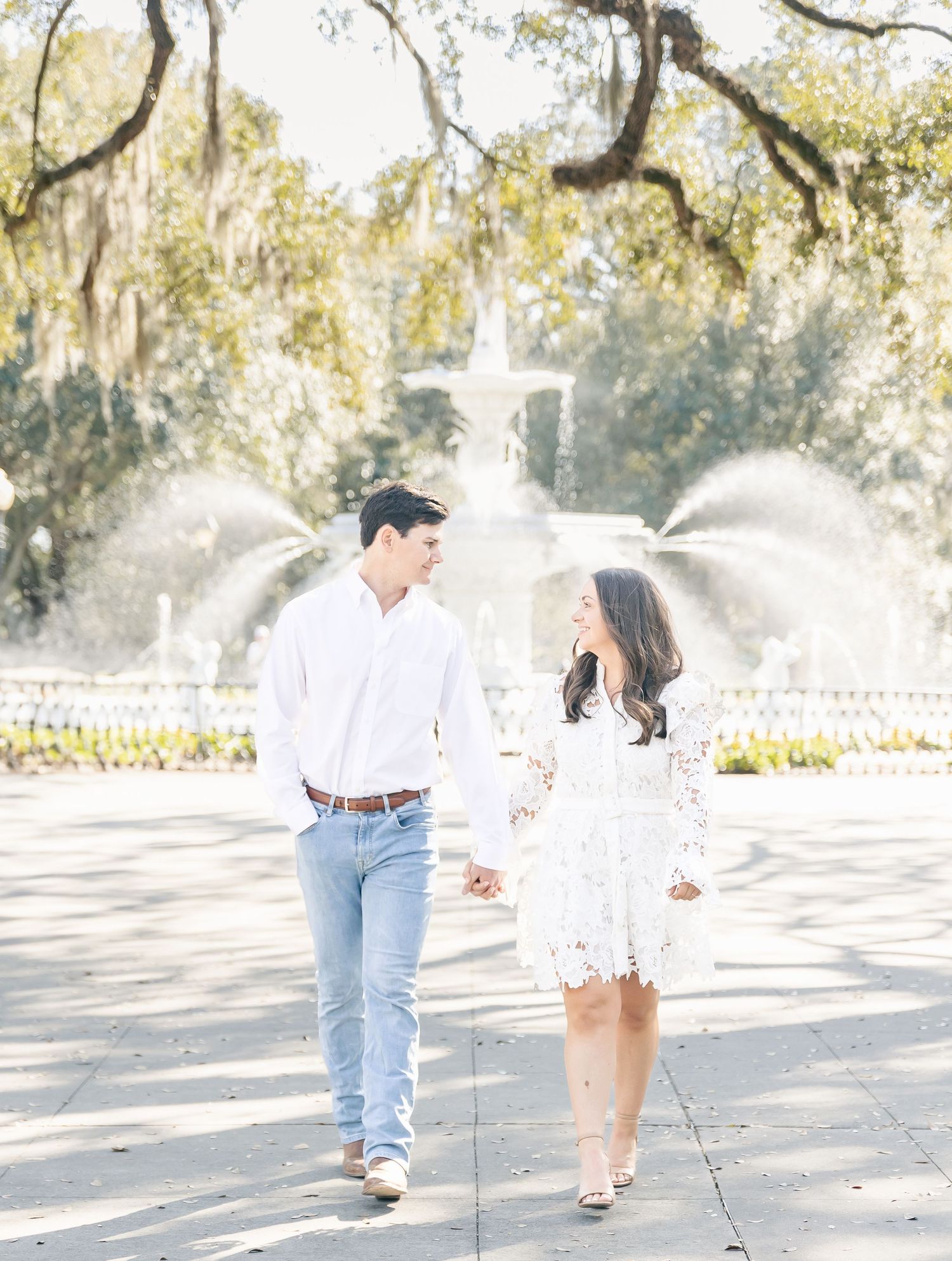 Couple walking together near fountain with Spanish moss draped trees in background.