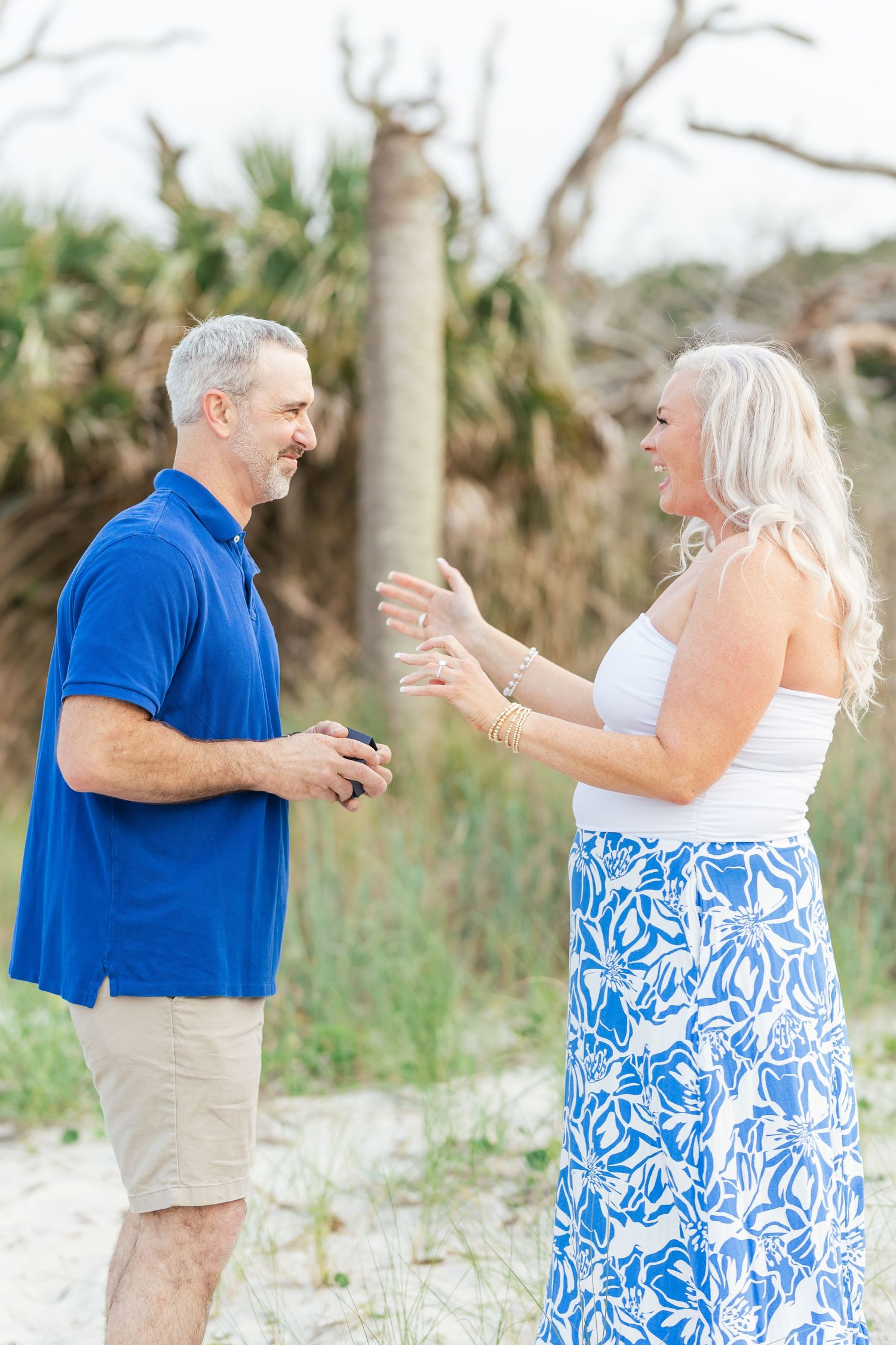 A couple shares an animated conversation while standing on a sandy beach path.