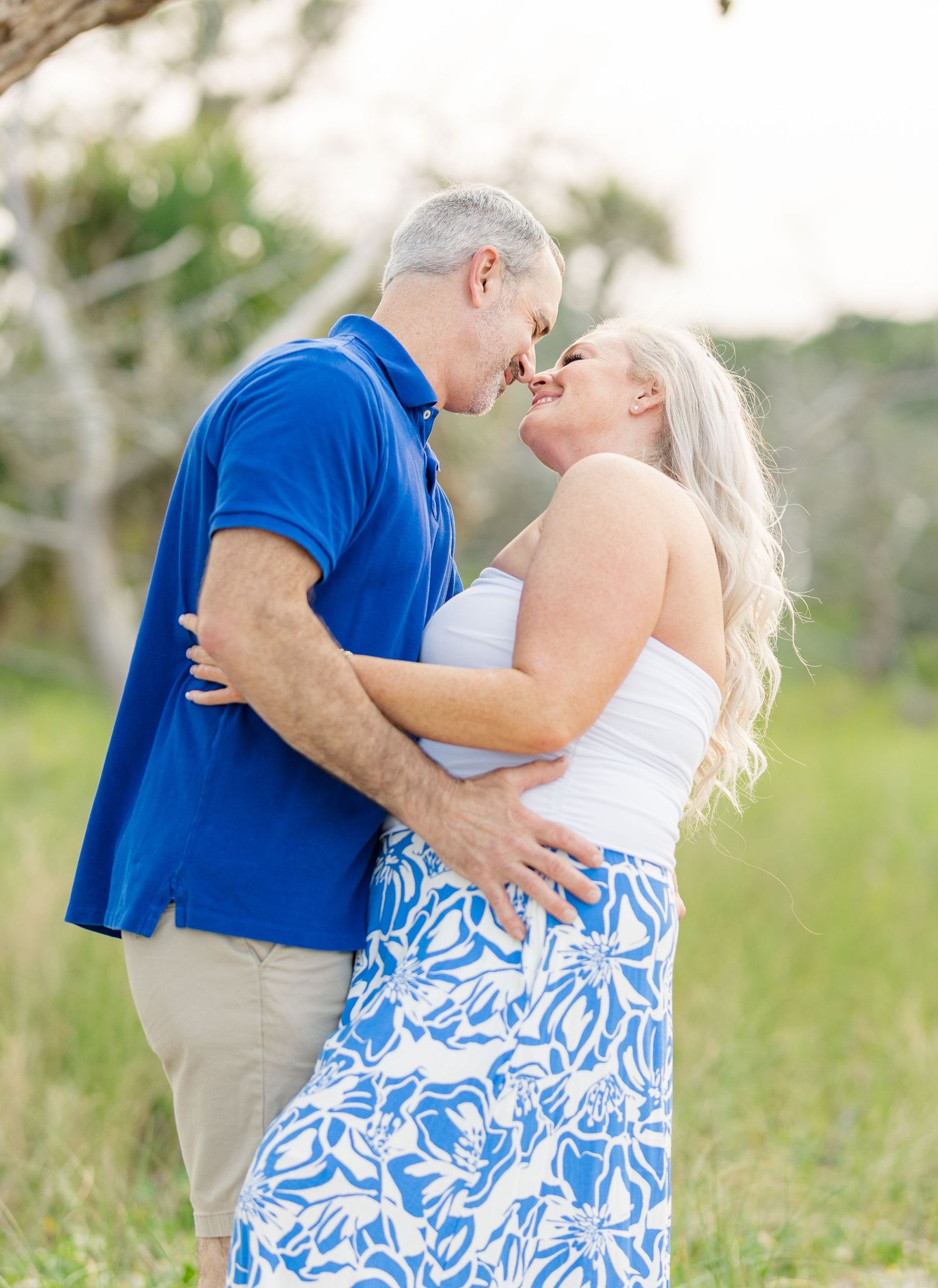 A couple embraces tenderly in a romantic outdoor setting wearing coordinating blue and white outfits.
