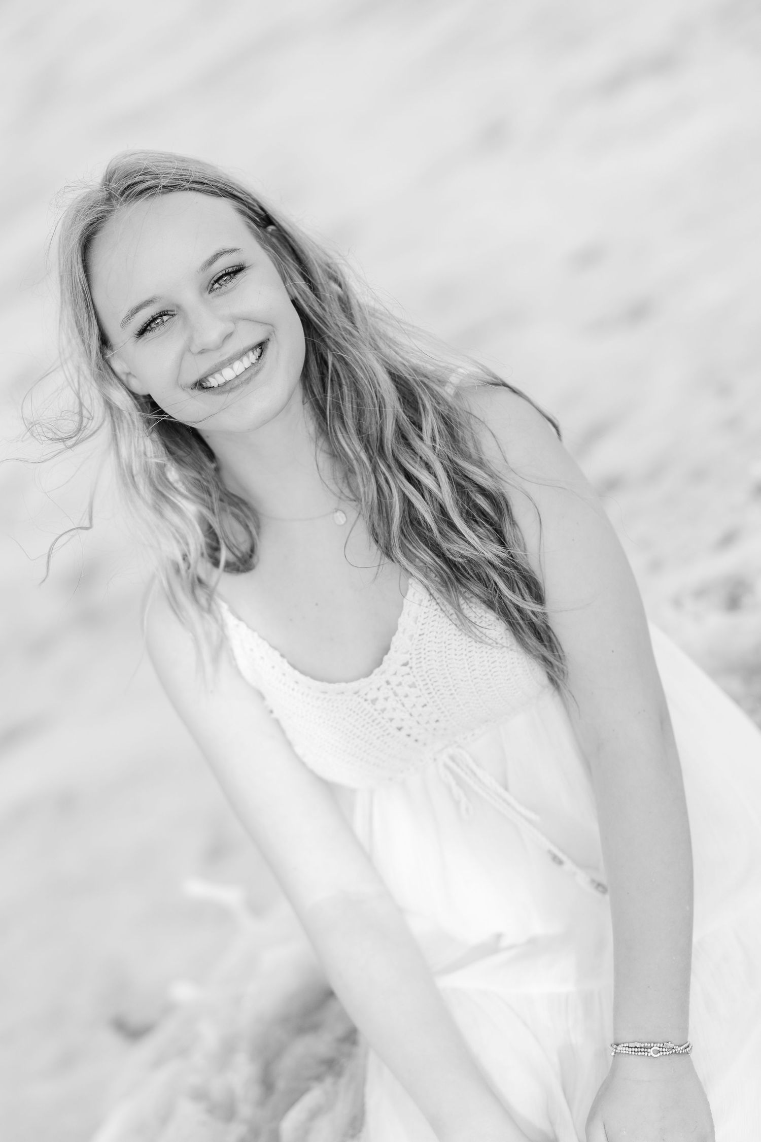 A bright and airy beach portrait showcases flowing blonde hair and a white summer dress against soft sand.