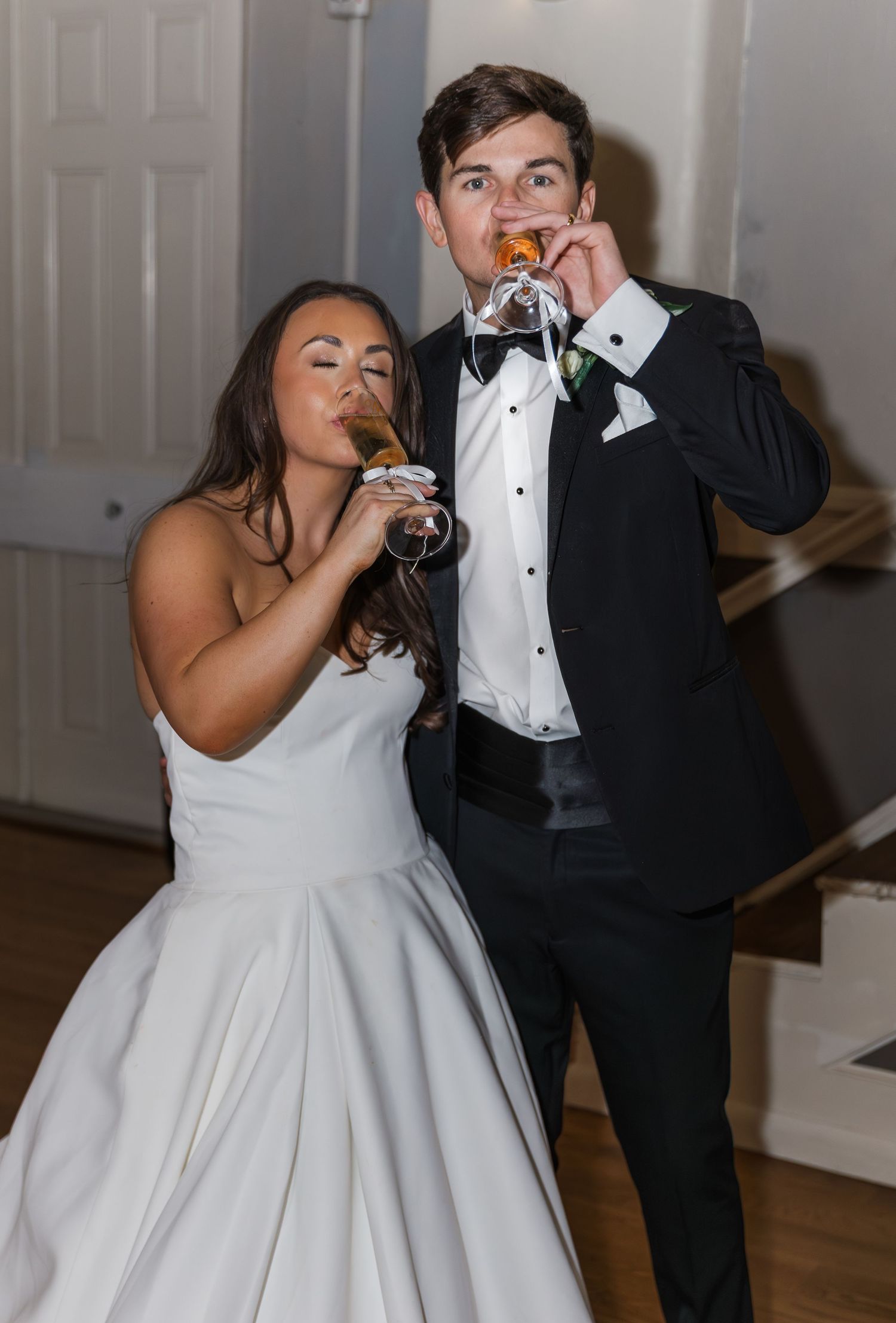 A couple in wedding attire shares drinks together at their reception.