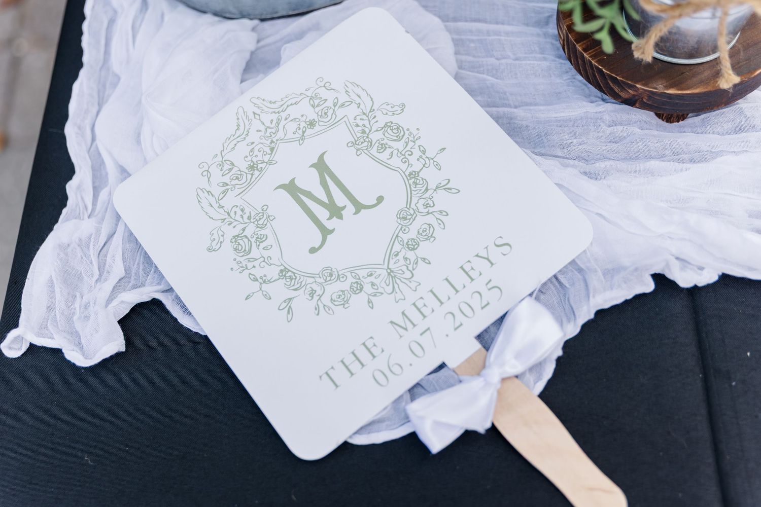 Wedding invitation suite with sage green monogram design and white envelopes arranged on dark surface.