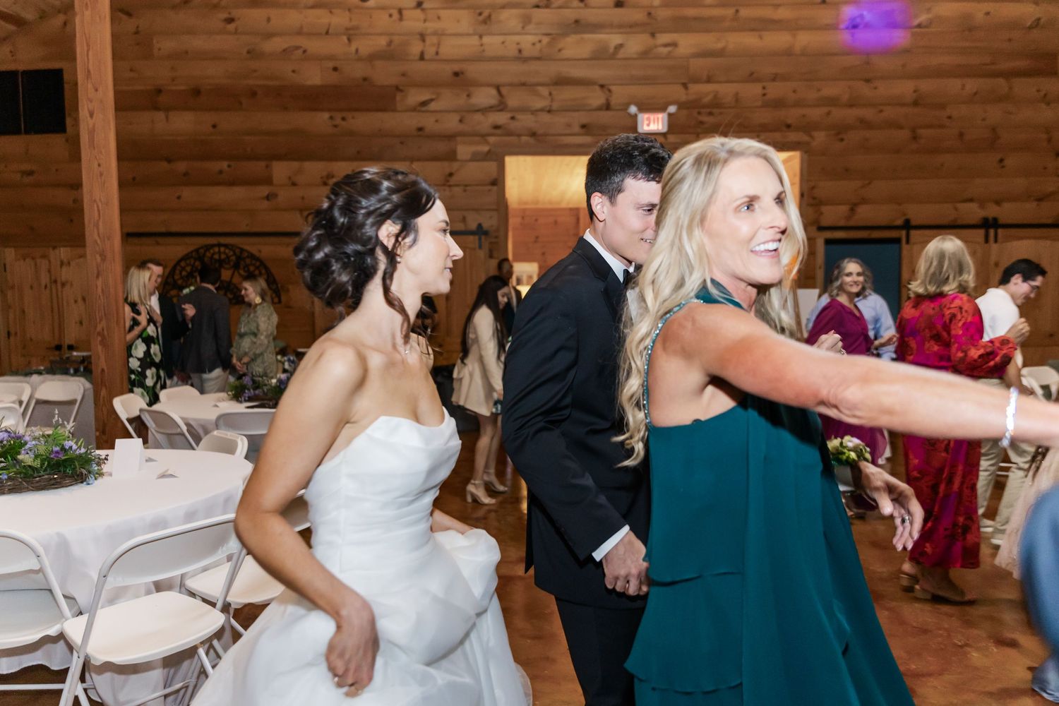 Guests dance and celebrate on the wooden dance floor of a rustic barn wedding venue.