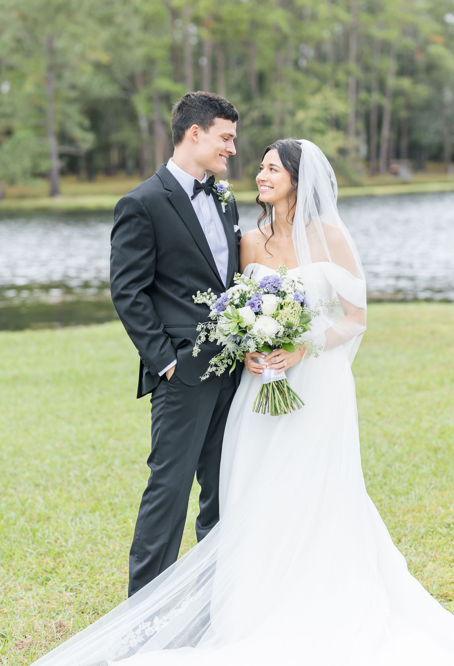 Romantic wedding couple shares intimate moments in an outdoor setting with lake and trees in background.