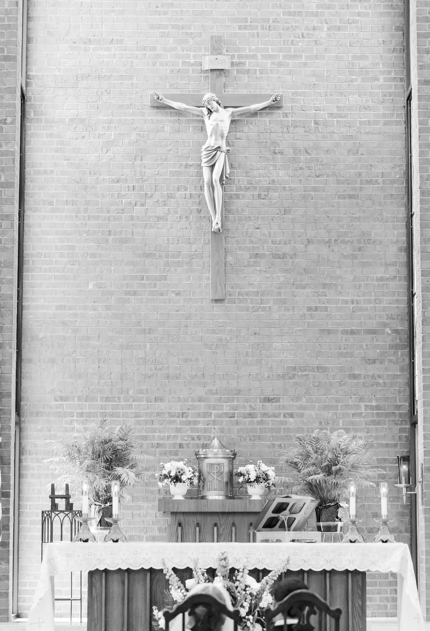 Black and white photo of a church altar with crucifixes and floral arrangements against brick walls.
