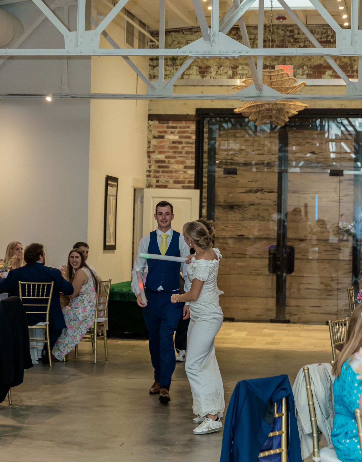 Wedding party members dance and celebrate in an industrial-style venue with exposed brick walls.