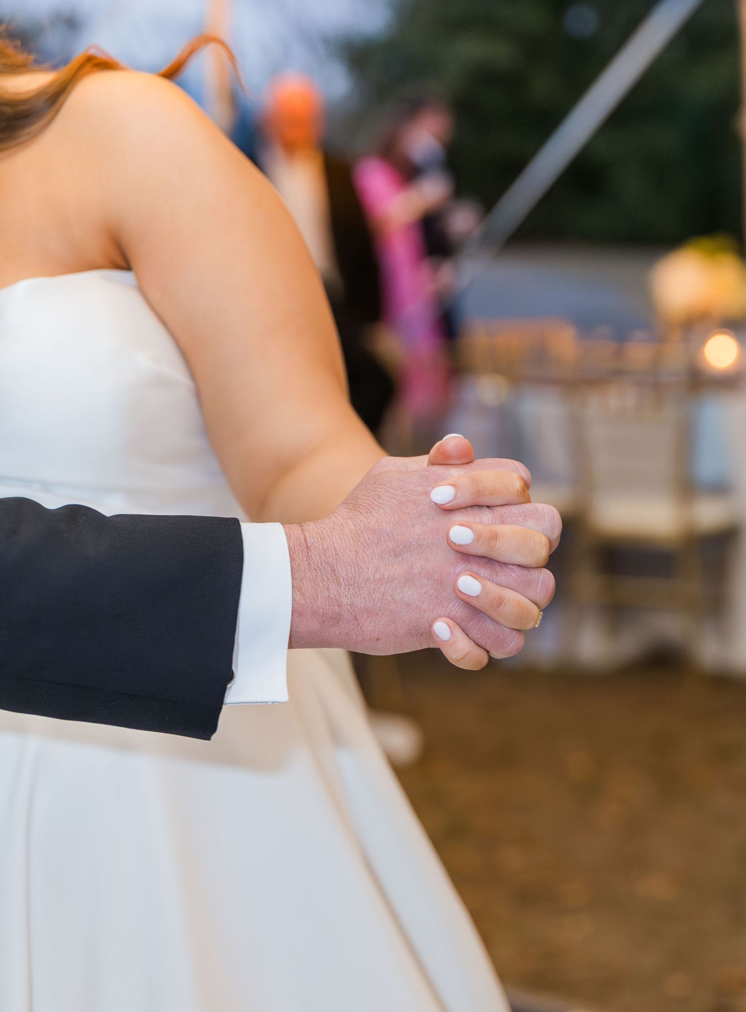 Close-up of bride and groom holding hands during their first dance at an outdoor wedding reception.