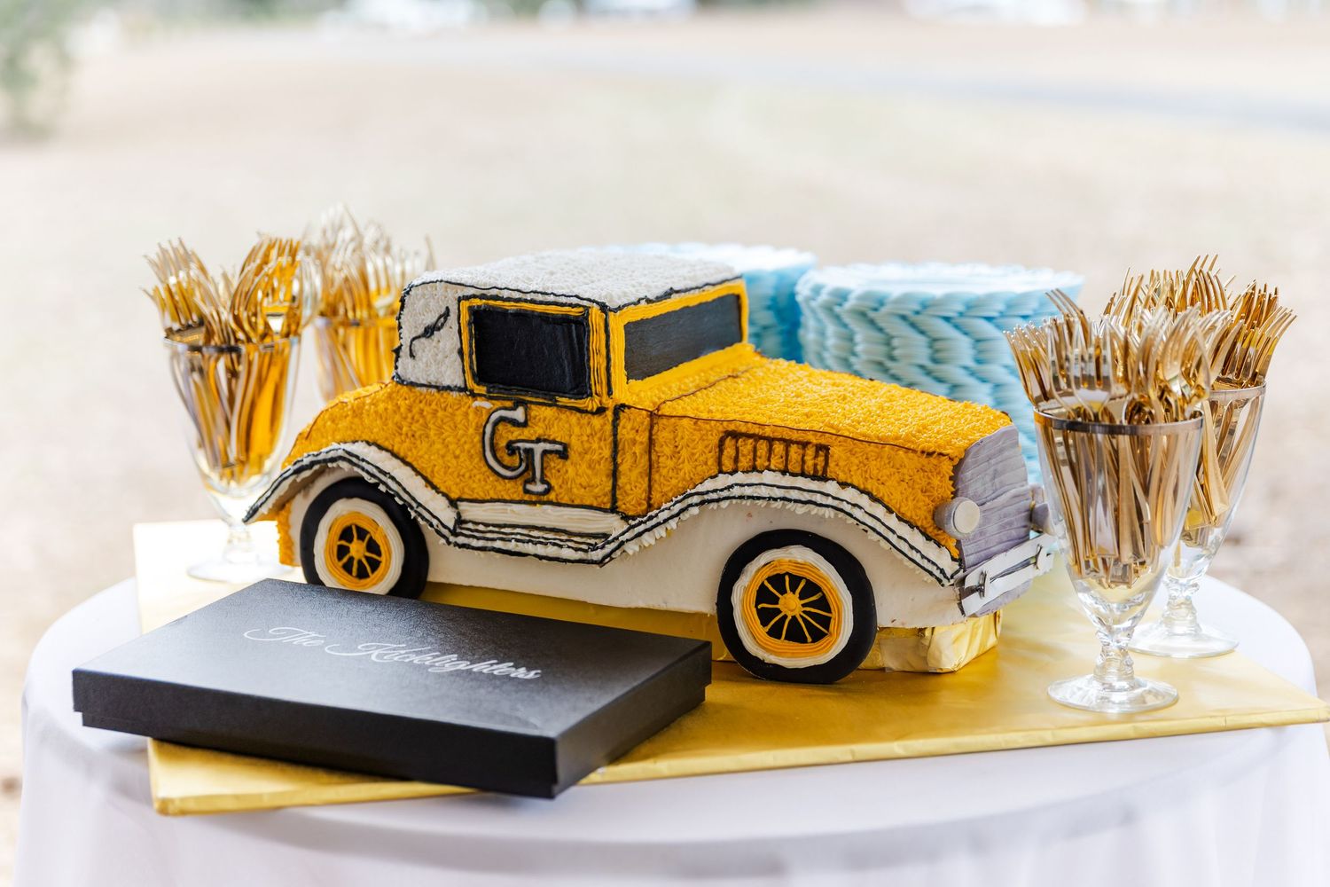 Georgia Tech themed groom's cake shaped as a vintage yellow Ramblin Wreck car with gold fork displays.