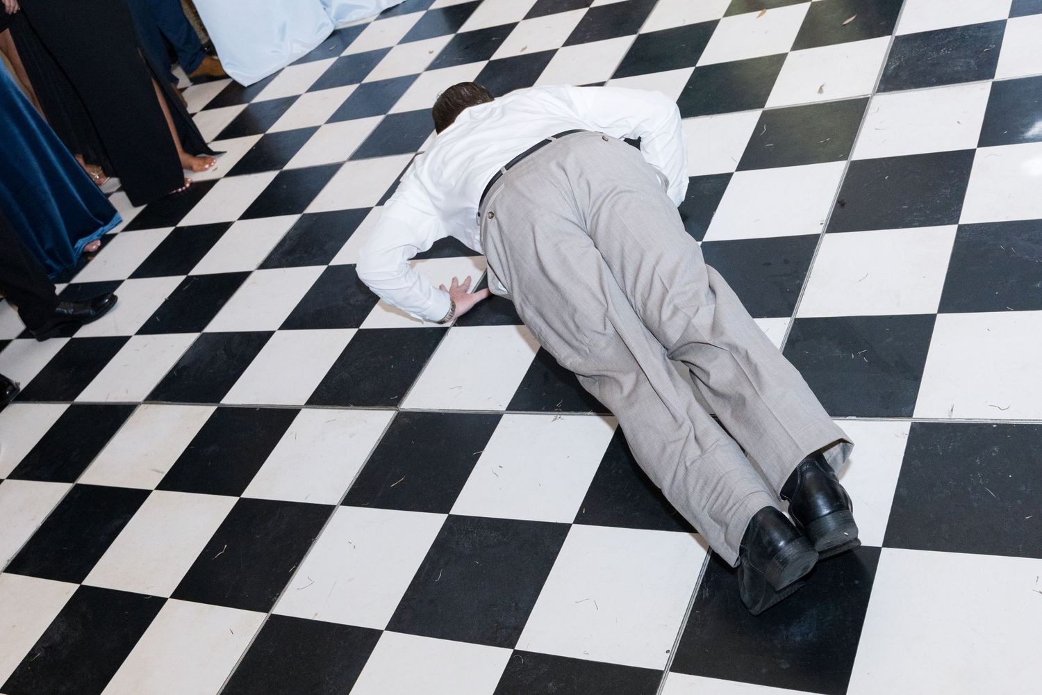 Wedding guest lying flat on black and white checkered dance floor during lively reception party.
