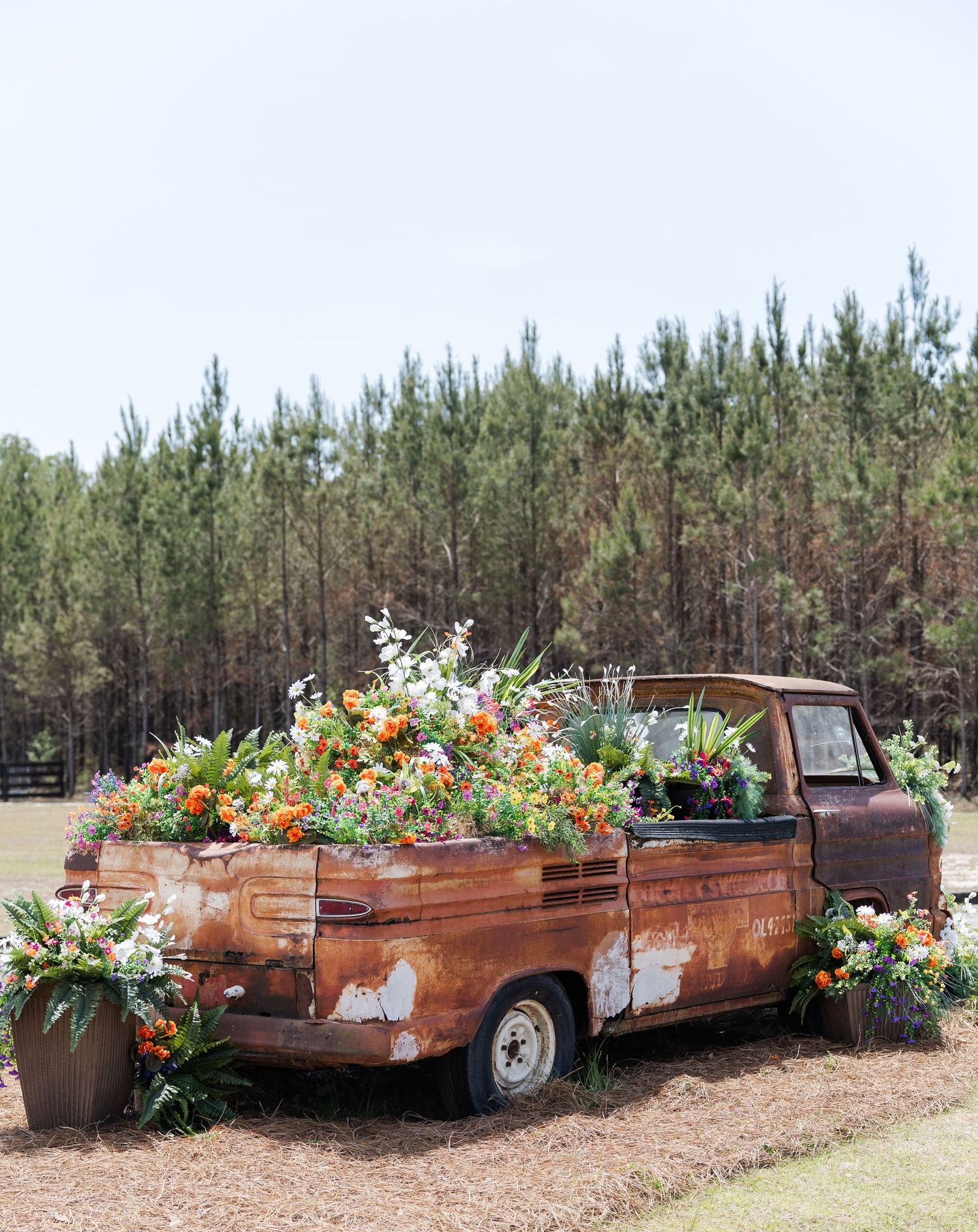 Rustic vintage truck filled with colorful floral arrangements used as wedding decor outdoors.