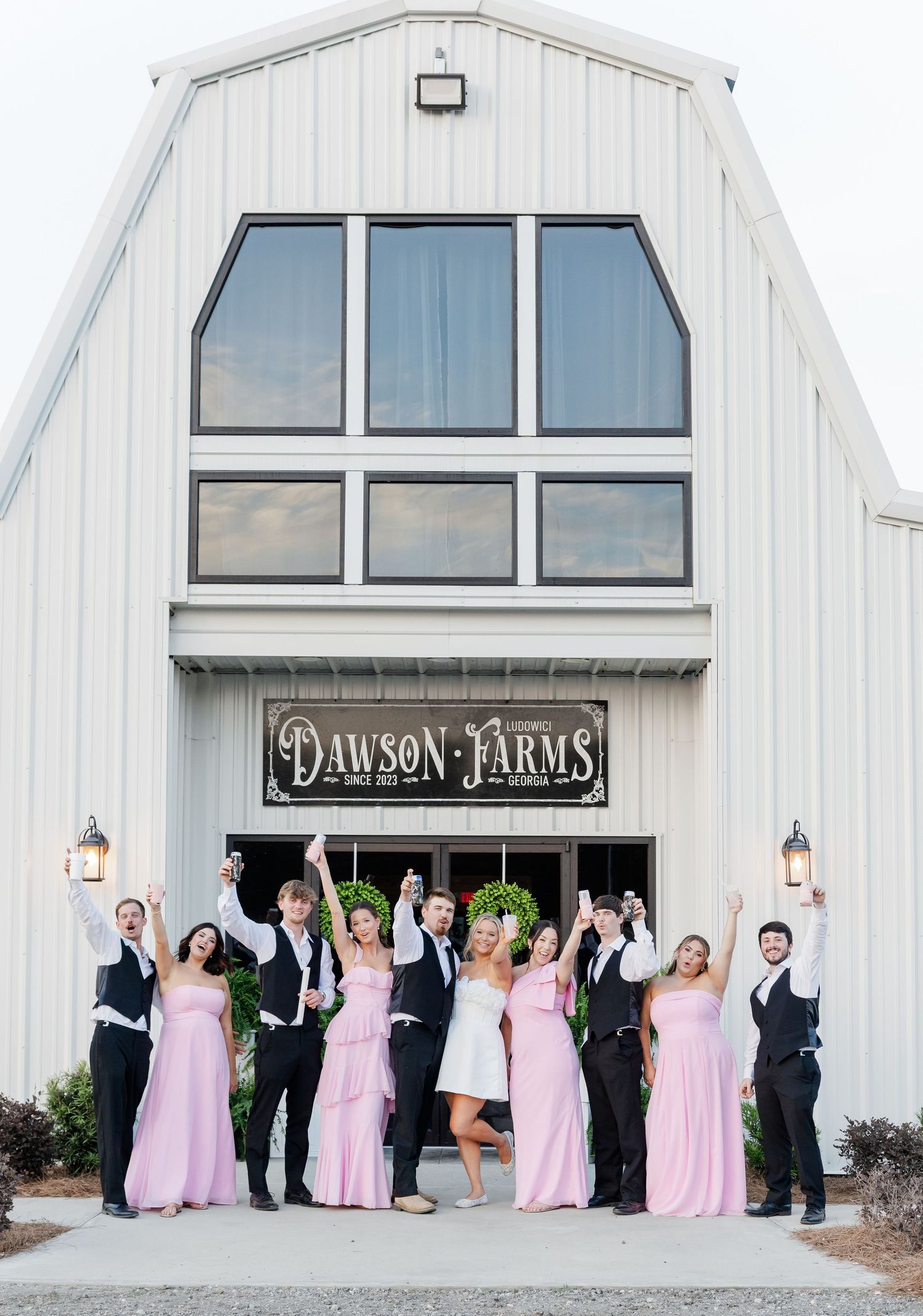 Wedding party celebrating outside Dawson Farms barn venue, bridesmaids in pink gowns and groomsmen in black tuxedos.