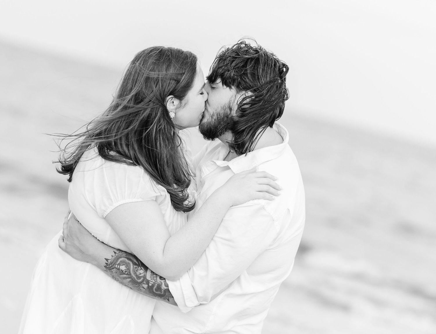A black and white intimate portrait of a couple kissing on the beach.