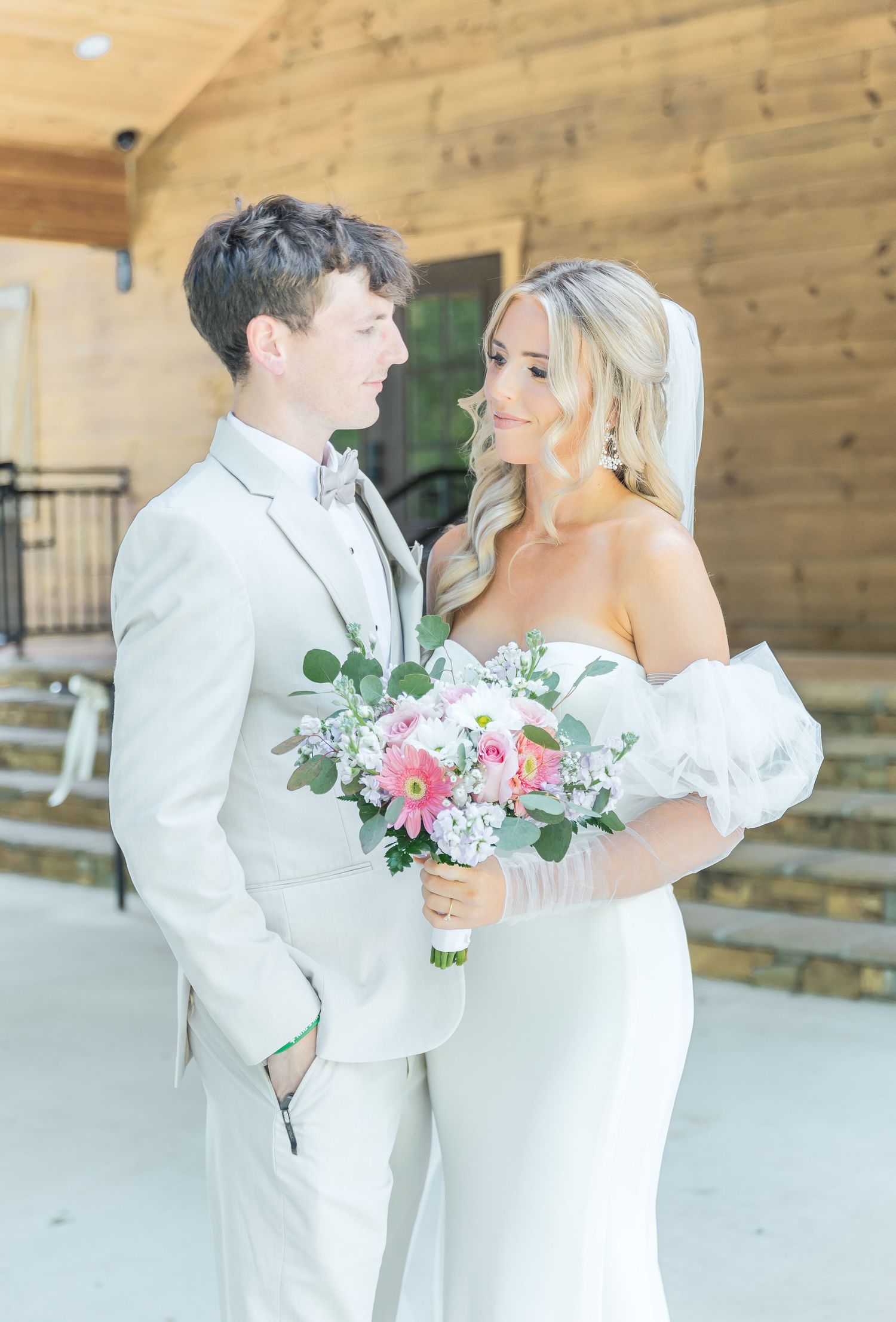 Romantic wedding portrait of couple in white attire gazing at each other with pink bouquet.
