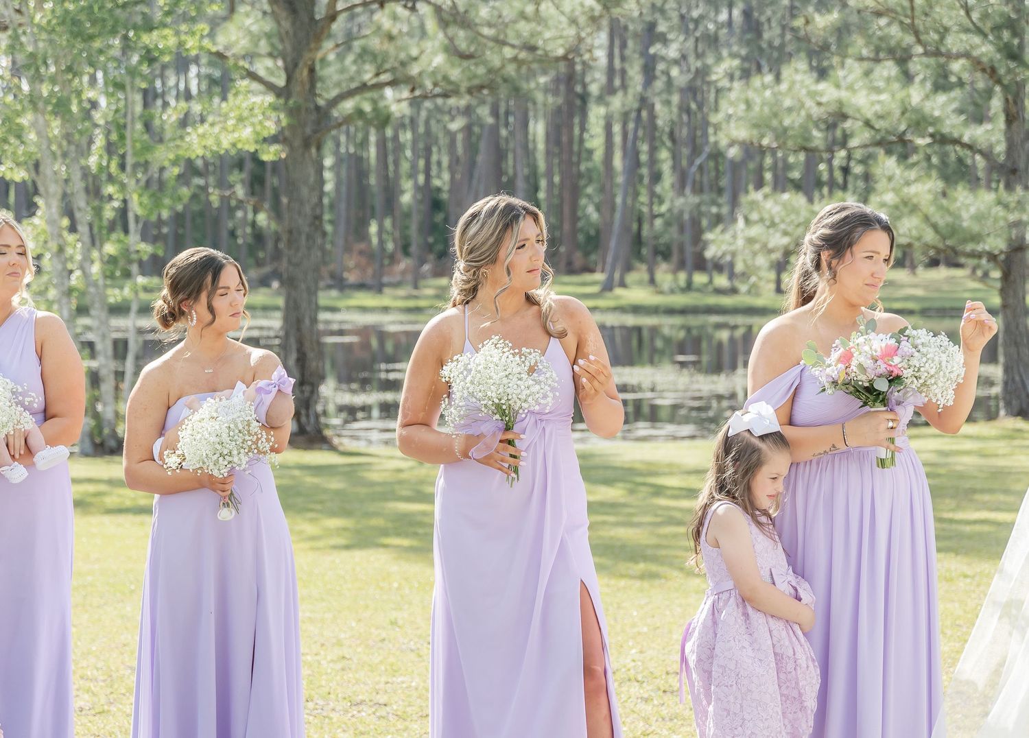 Bridesmaids in flowing lavender dresses holding bouquets at an outdoor wedding ceremony.