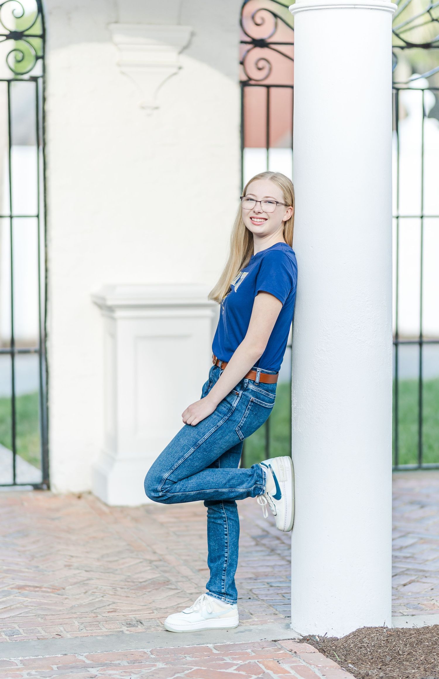 Person in blue t-shirt and jeans poses casually against white column in outdoor setting.