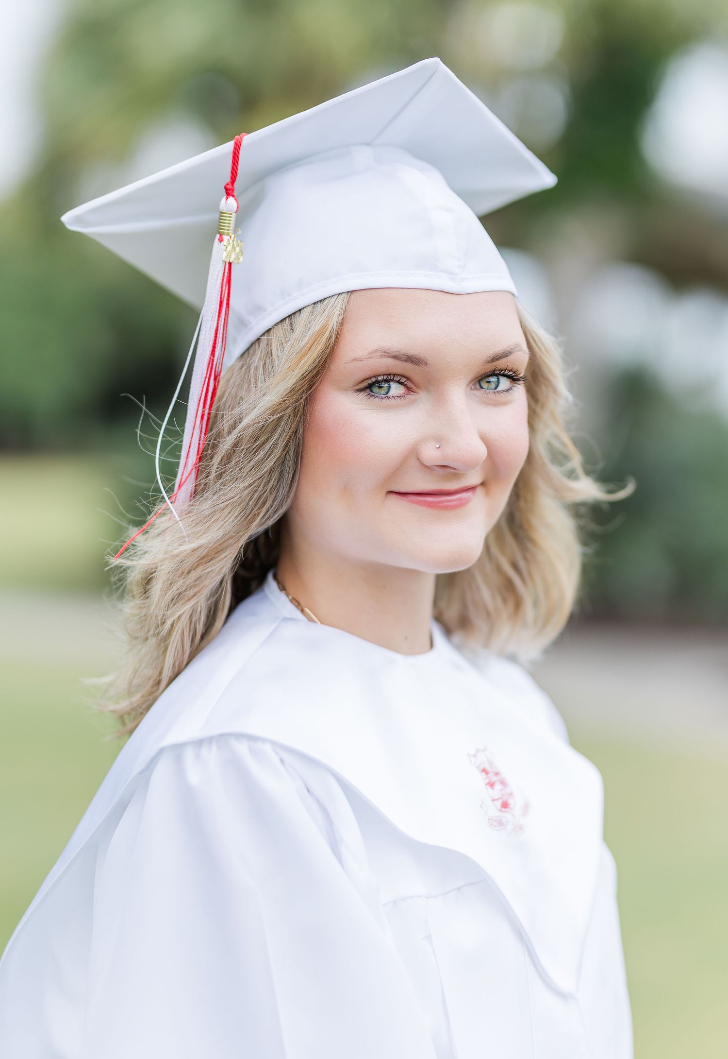 Graduate wearing white cap and gown with red tassel smiles at camera.
