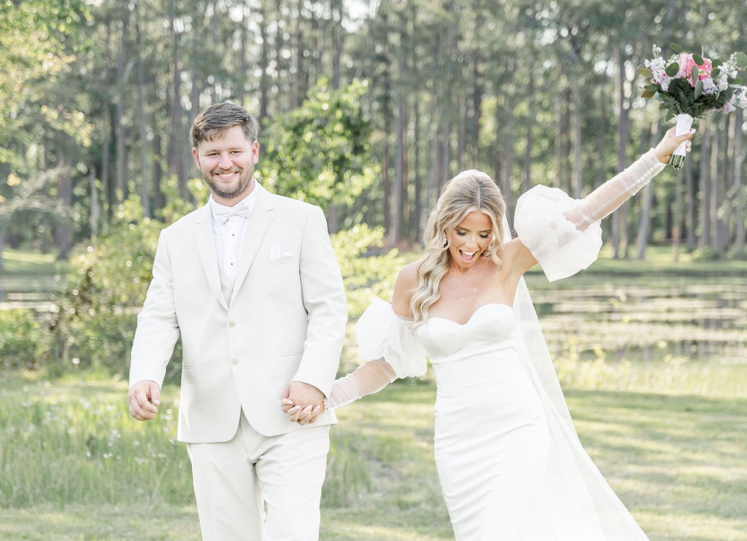 Happy newlyweds holding hands while bride raises bouquet in celebratory pose outdoors.