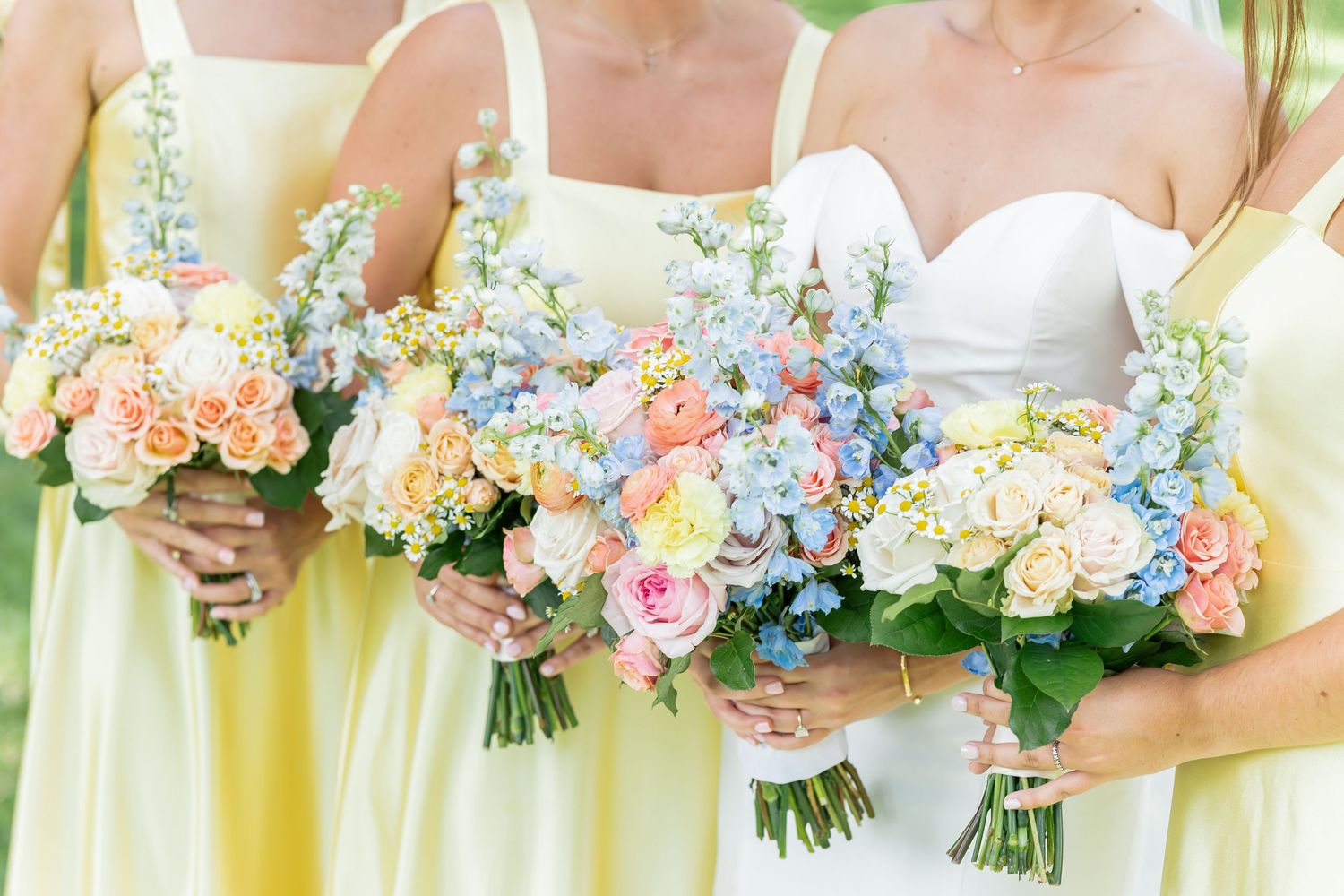 Row of pastel bouquets featuring blue hydrangeas and peach roses held by bridesmaids.