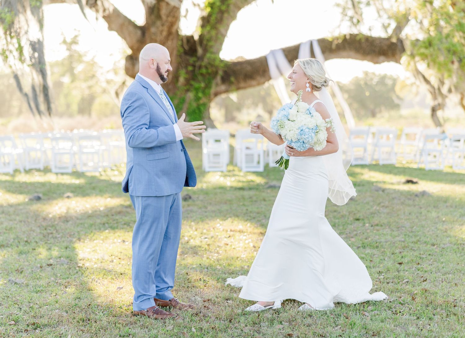 Bride in white gown and groom in light blue suit share an emotional first look outdoors.