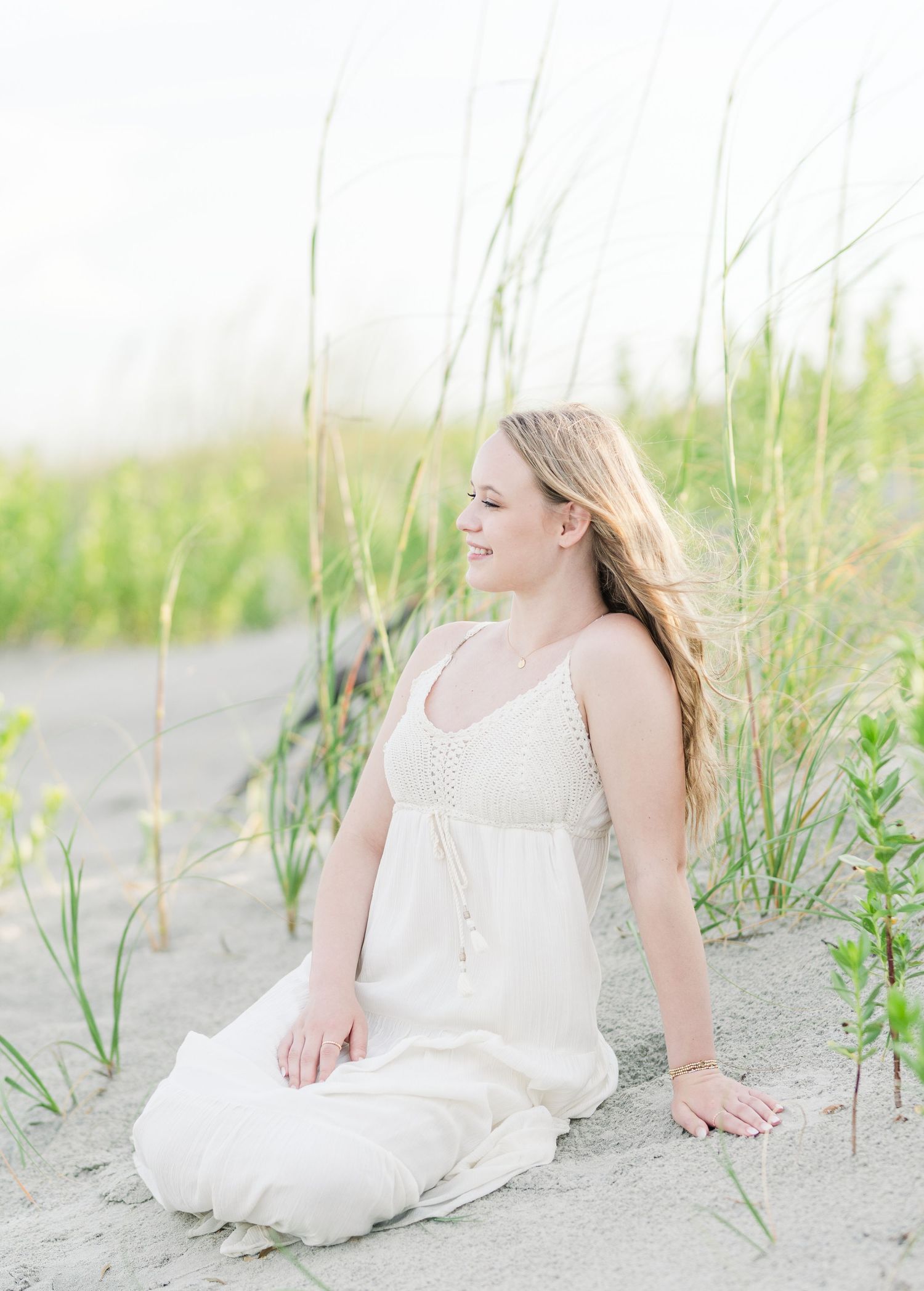 A dreamy coastal portrait among beach grass with soft, ethereal lighting.