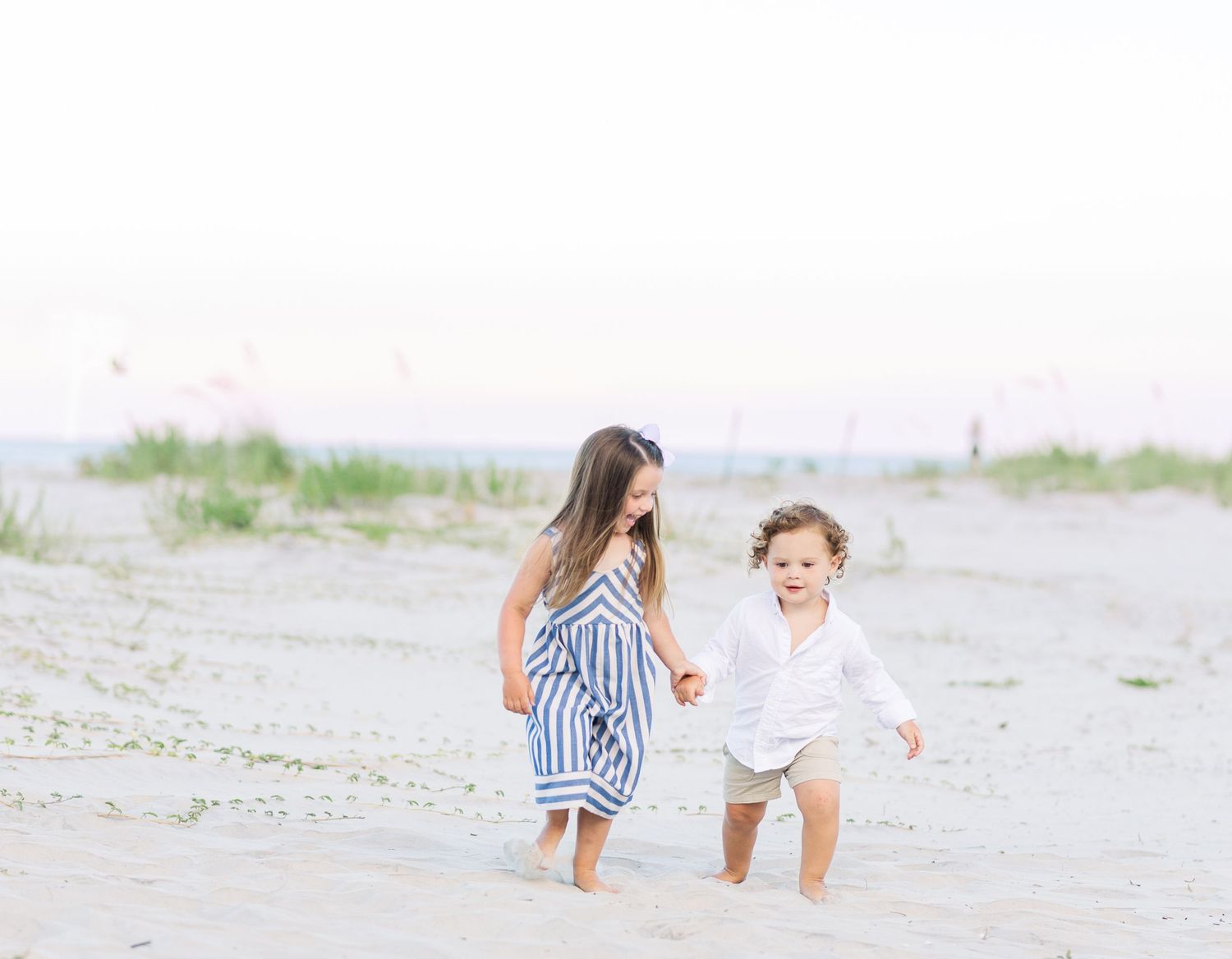People strolling together along a sandy beach on a sunny day wearing blue and white striped clothing.