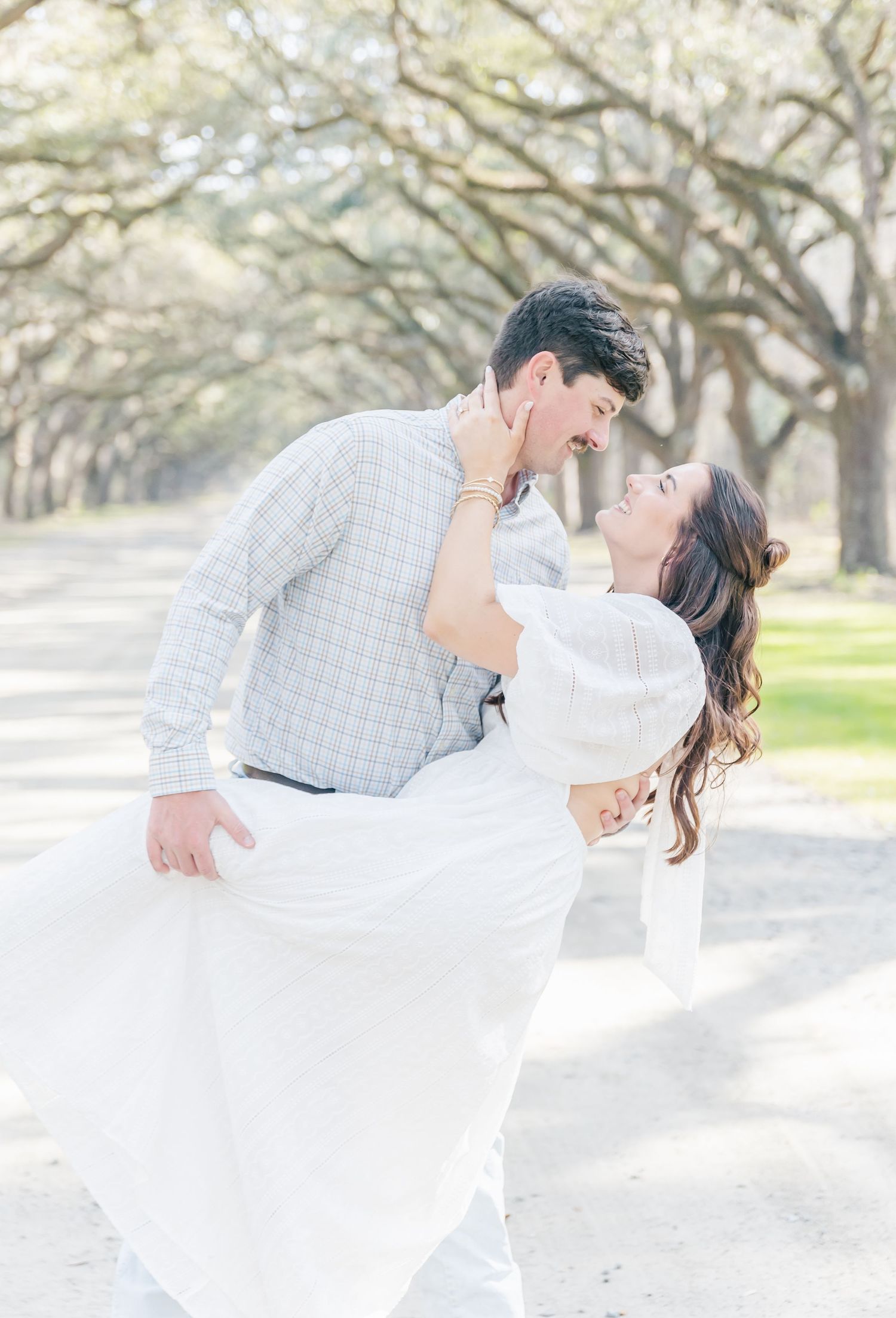 A romantic couple shares a tender moment under an archway of oak trees.