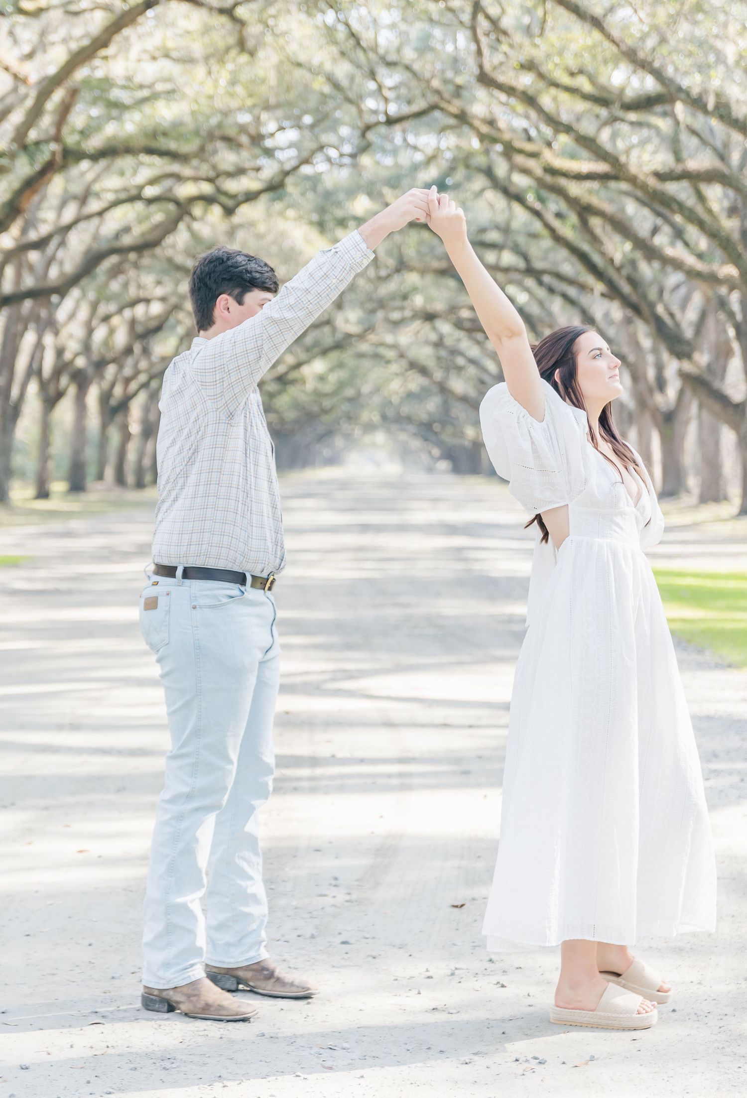 A couple perform a romantic dance move under a beautiful tree-lined avenue.