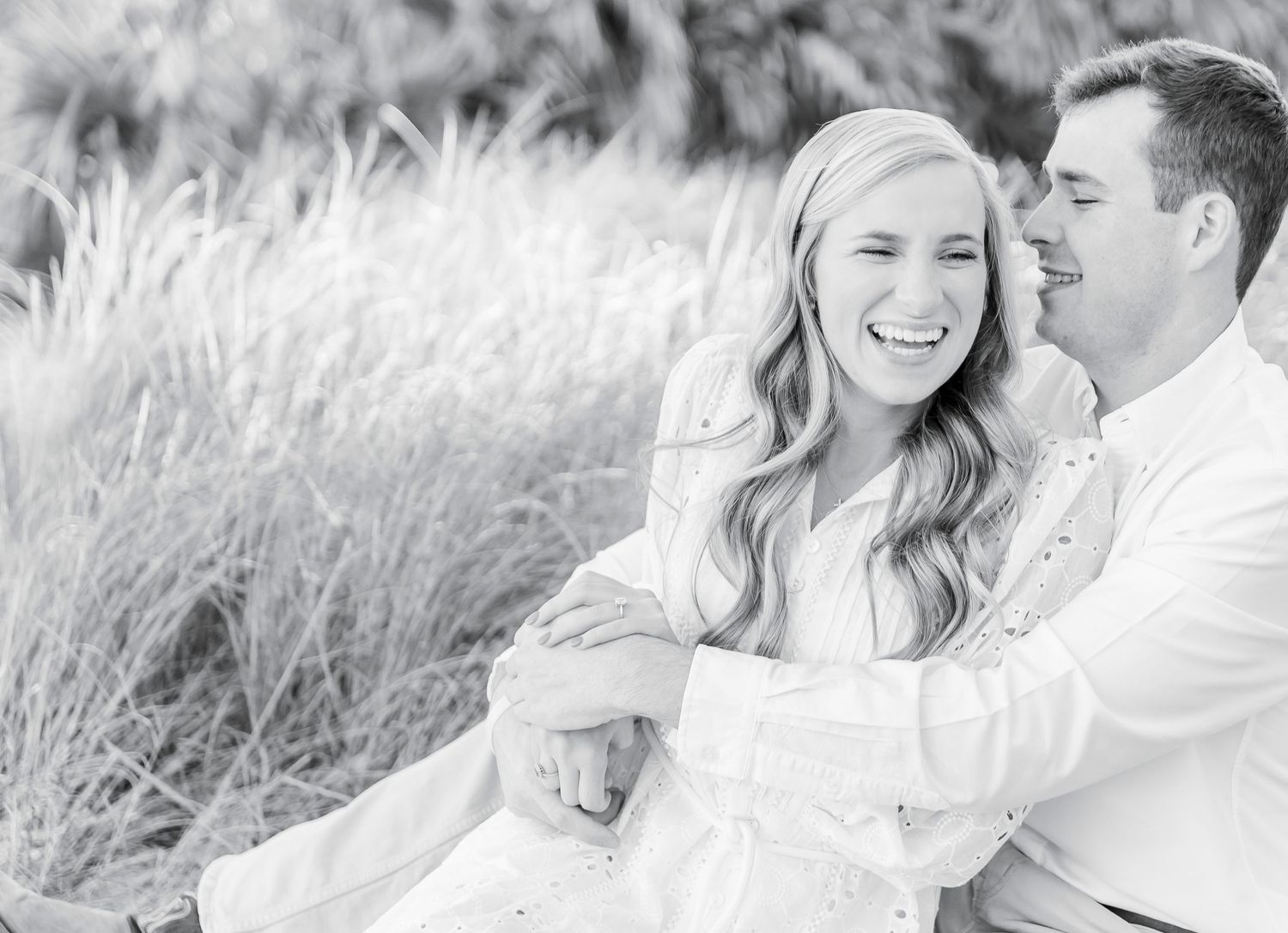 A joyful couple laughing together in a field of tall grass during sunset.