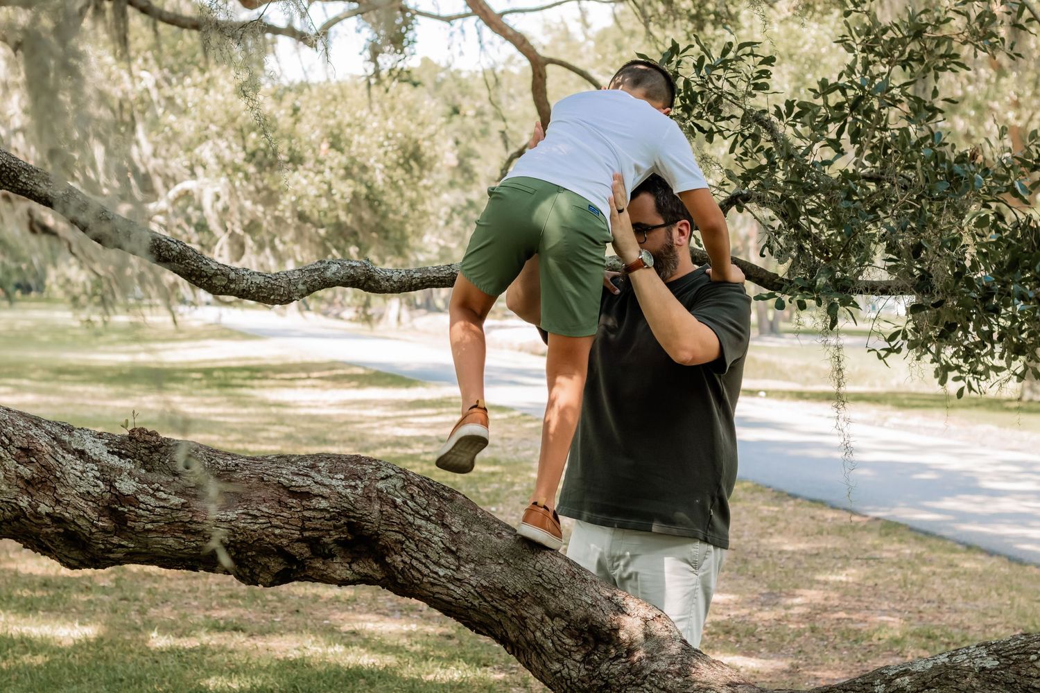 Two people playfully interacting with a large tree branch in a serene park setting under Spanish moss.