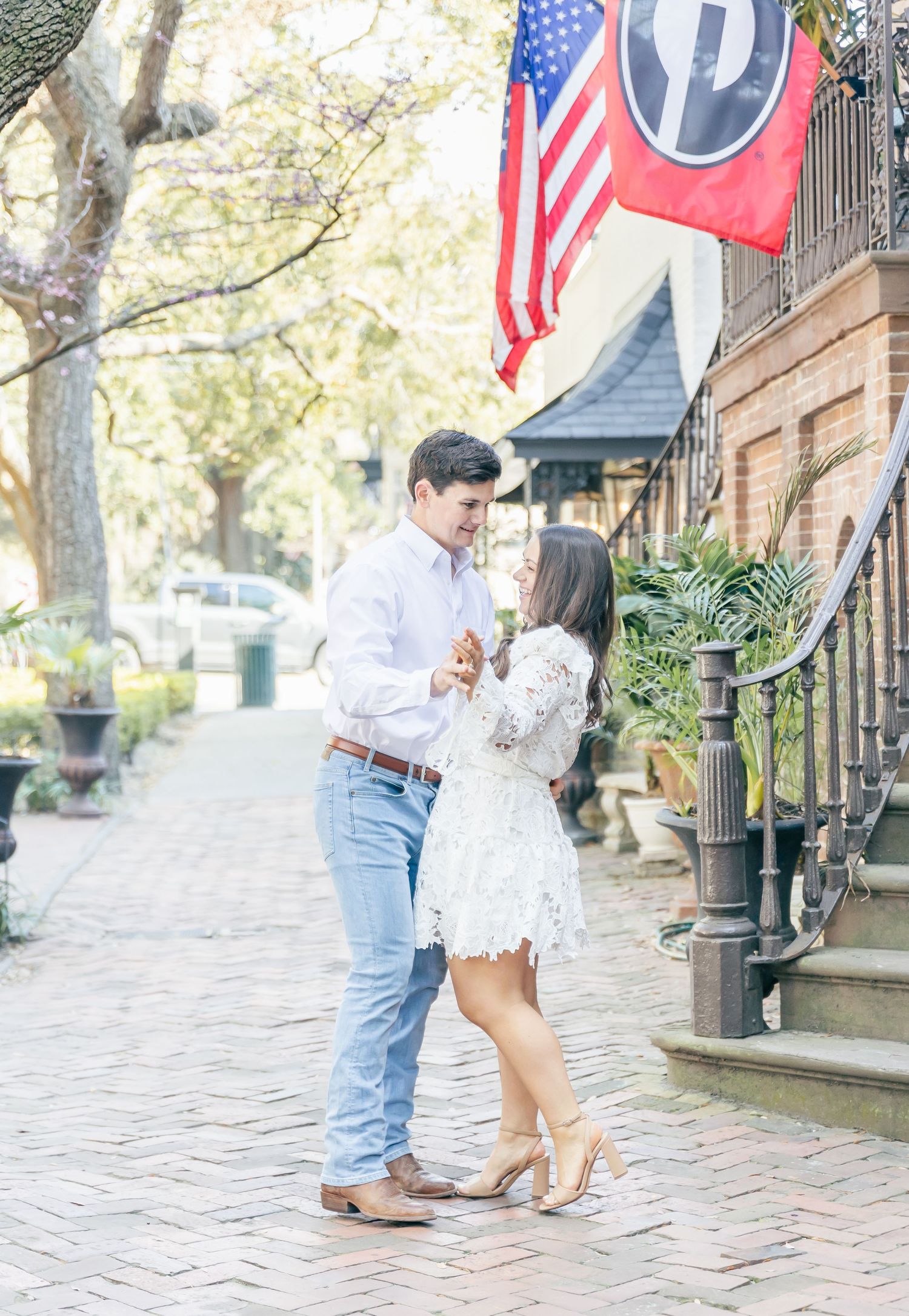 A romantic couple embraces on a historic brick pathway beneath hanging flags.