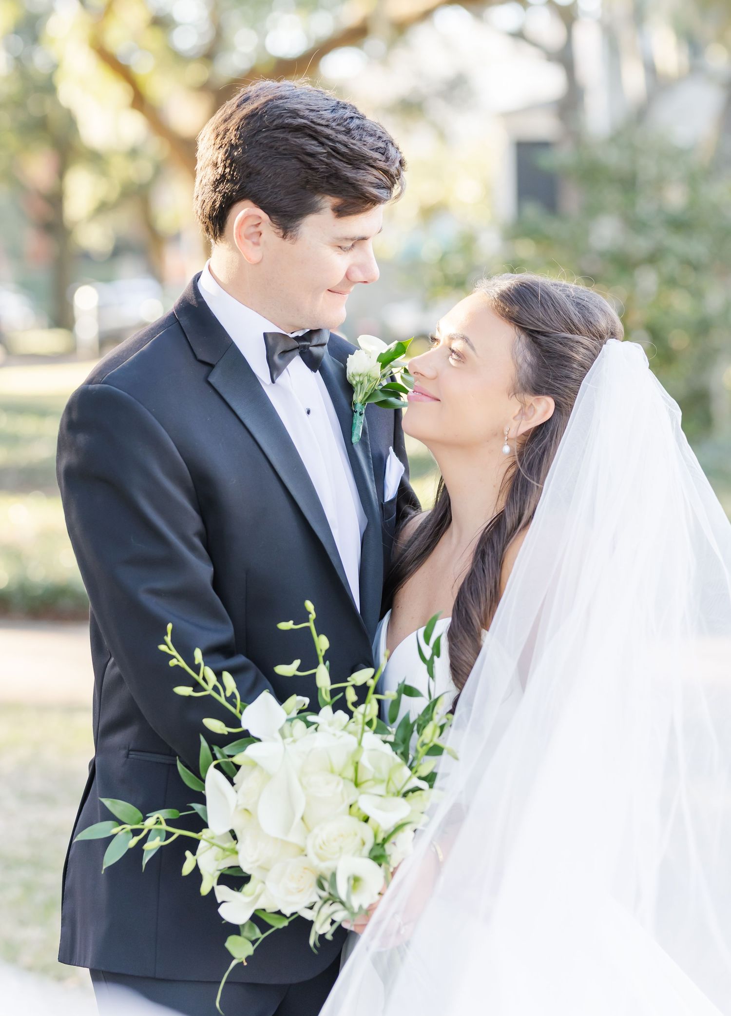 Romantic wedding couple shares intimate moments in an outdoor setting with elegant white floral bouquet.
