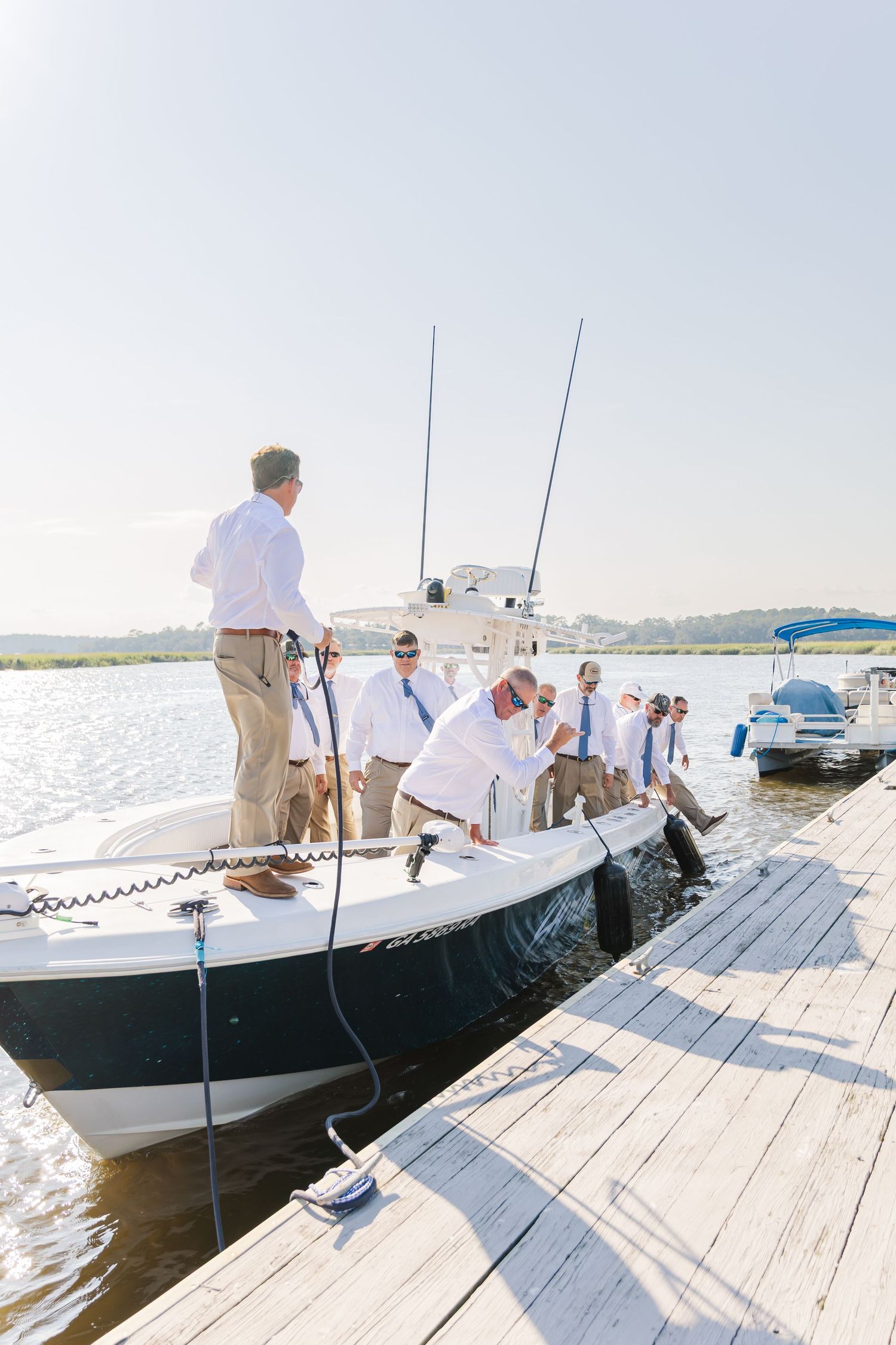 Several white boats moored at a wooden pier with people preparing for departure.
