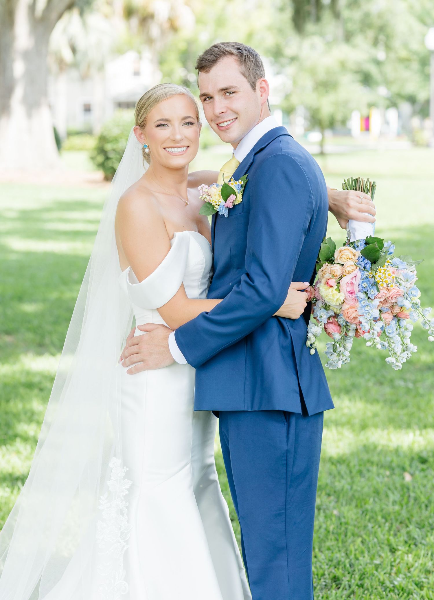 Couple dancing outdoors in wedding attire with colorful pastel bouquet in a garden setting.