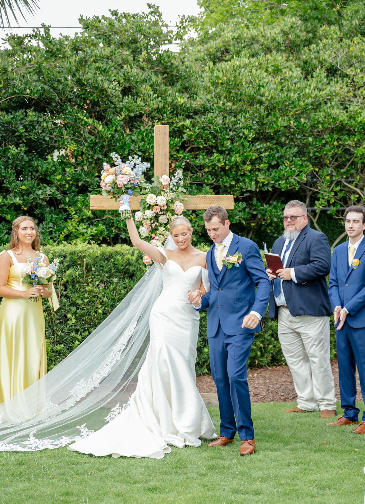 Wedding party poses in sequence for fun group photo on green lawn with flowing white dress and yellow accents.